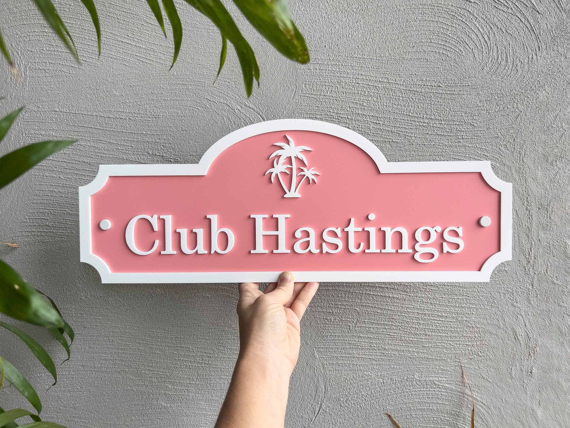 A tropical melon and white palm tree sign with 'Club Hastings'.