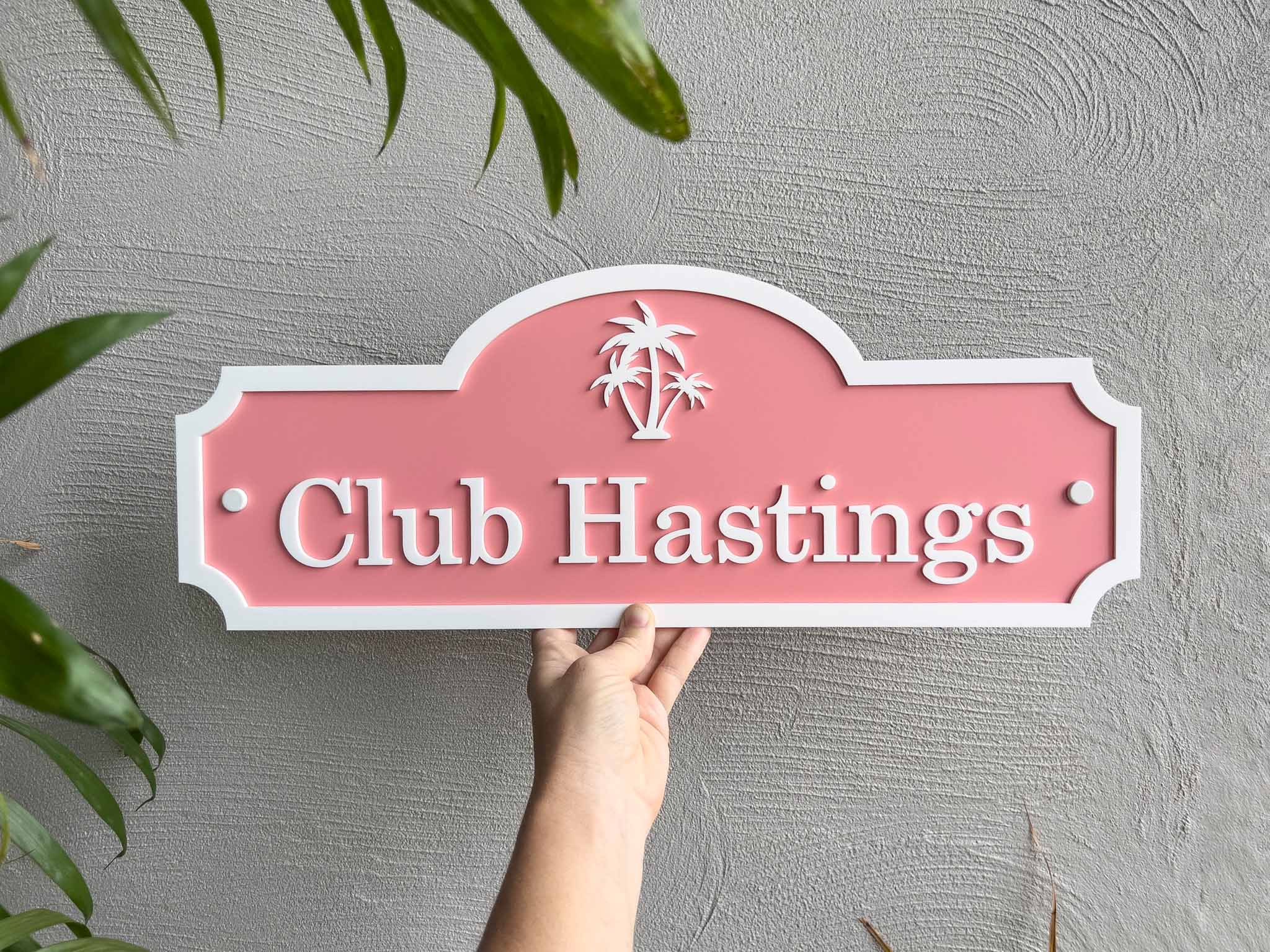 A tropical melon and white palm tree sign with 'Club Hastings'.