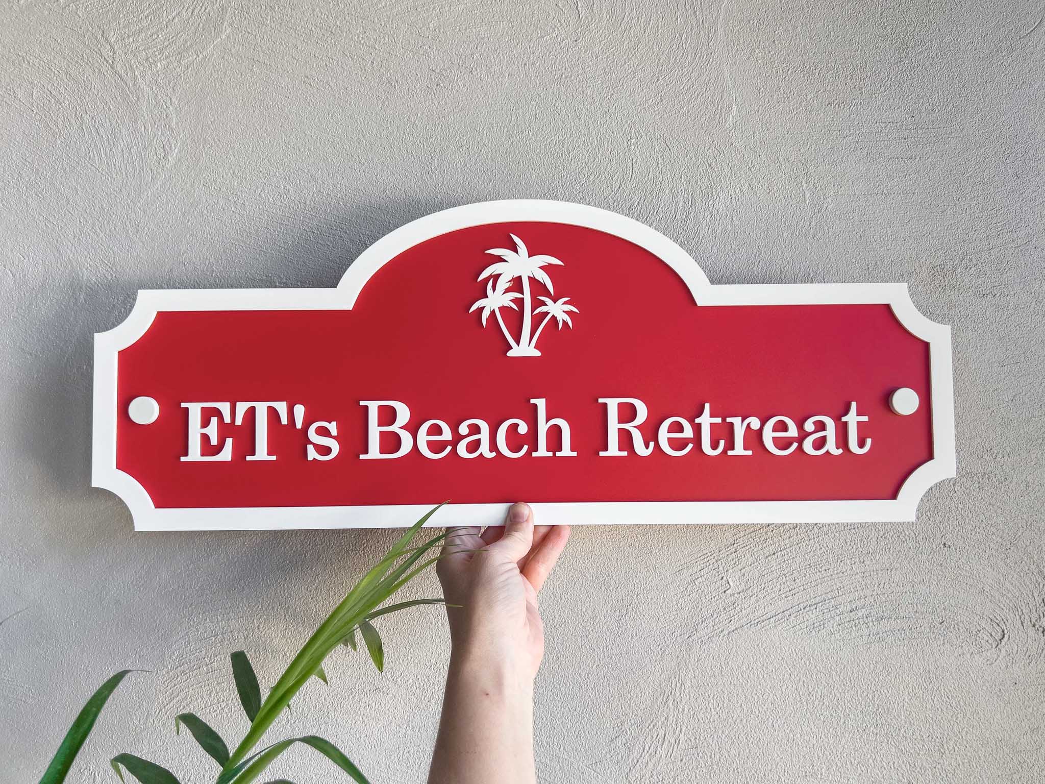 Red sign with 'ET's Beach Retreat' text and palm tree design held against a light gray wall.