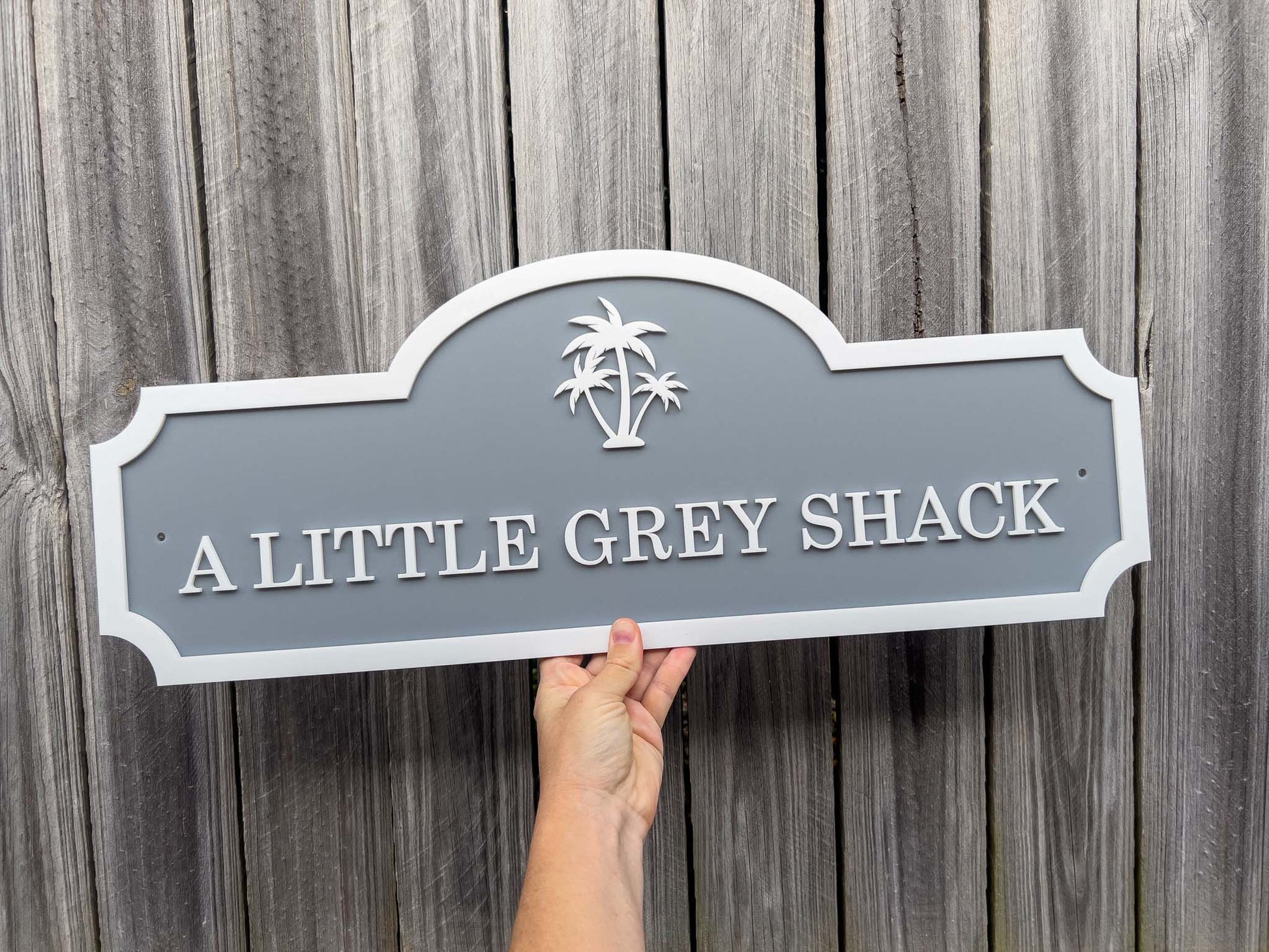 3D acrylic laser cut sign in grey and white with a palm tree that says the workds 'A LITTLE GREY SHACK'.