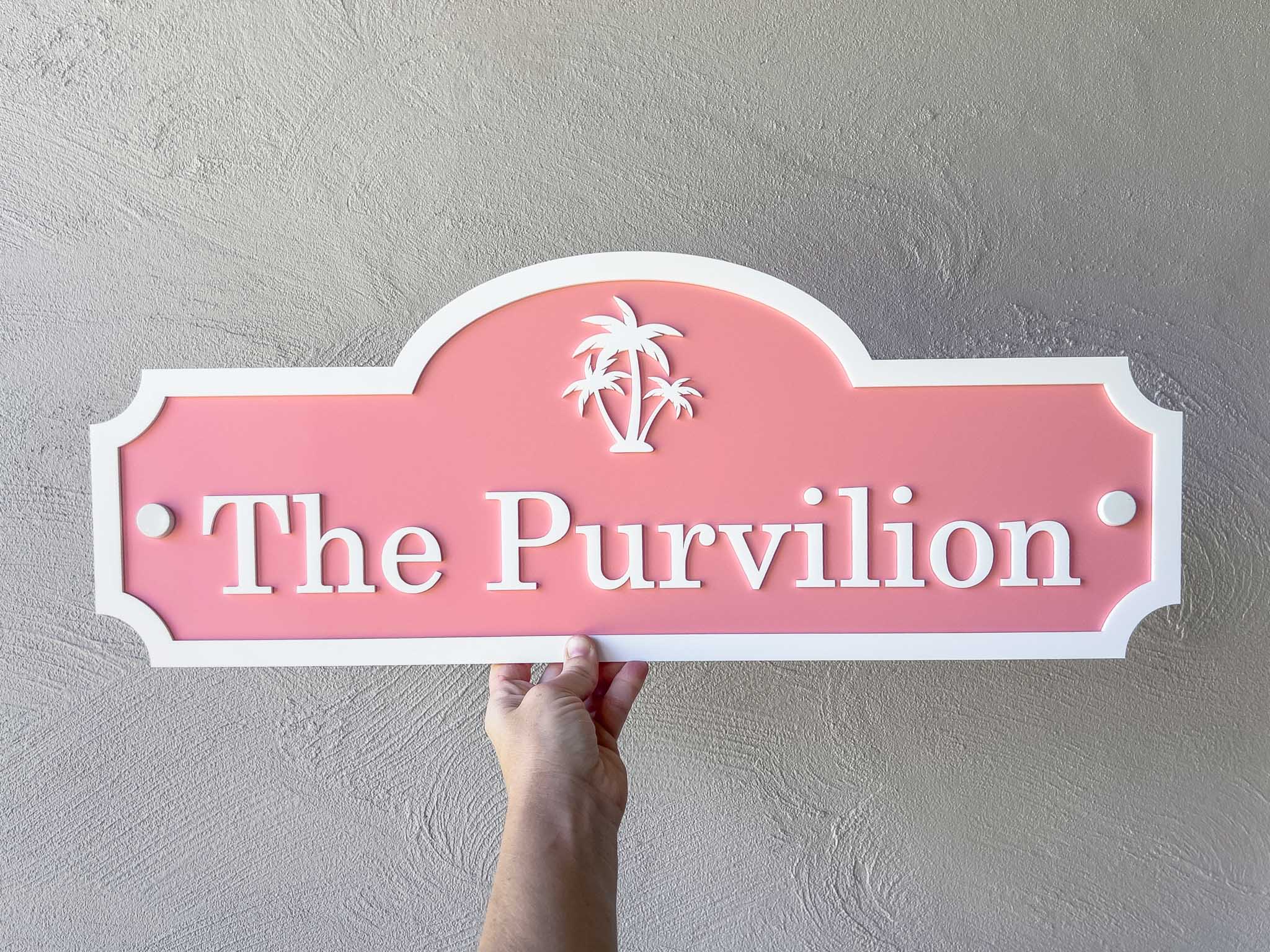 Pink sign with 'The Purvilion' text held against a gray wall