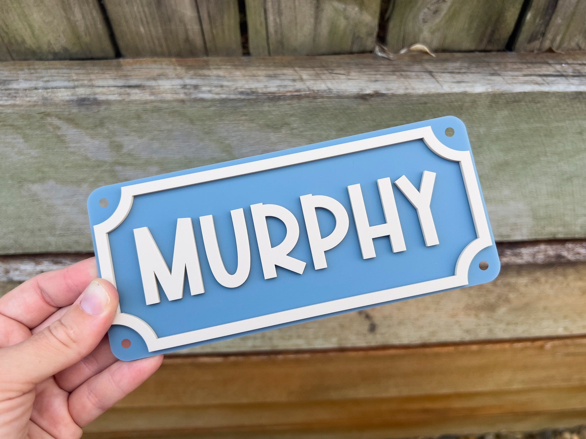 Hand holding a blue sign with 'MURPHY' on it against a wooden background