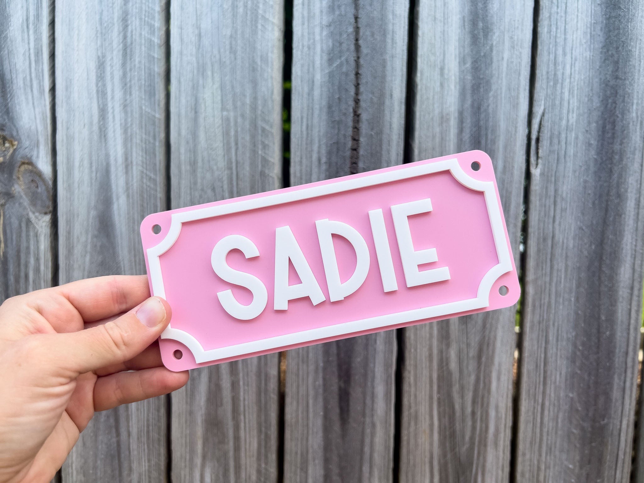 Hand holding a pink sign with 'SADIE' on a wooden background