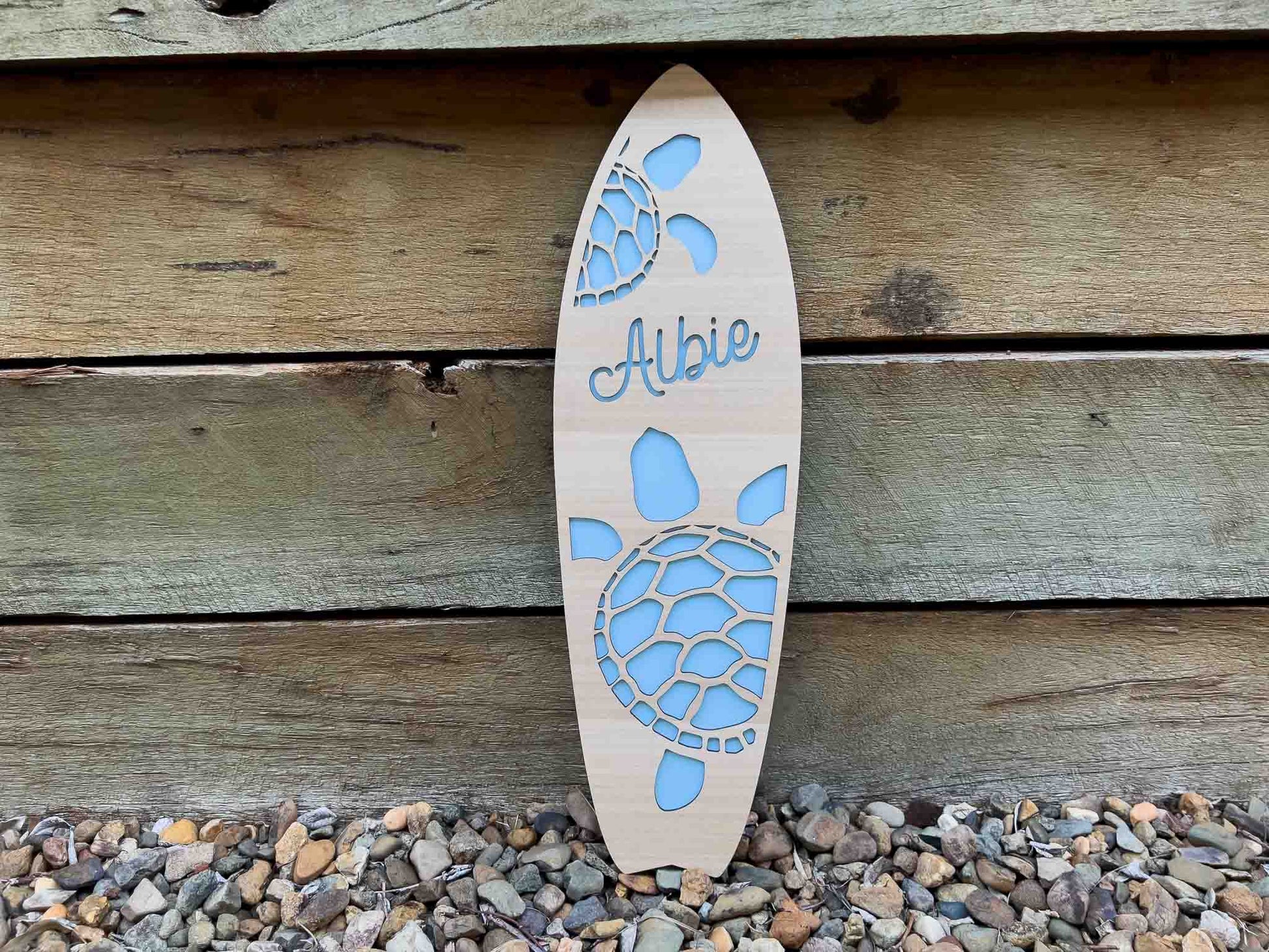 Wooden surfboard-shaped sign with turtle design and 'Albie' engraving on a wooden background.
