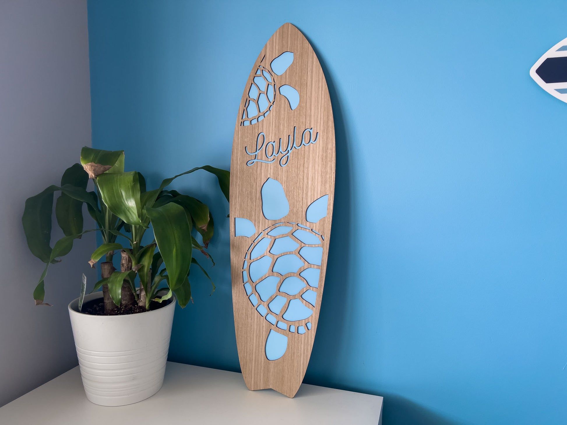 Timber surfboard name plaque in a child's bedroom that says 'Layla' with a blue background.