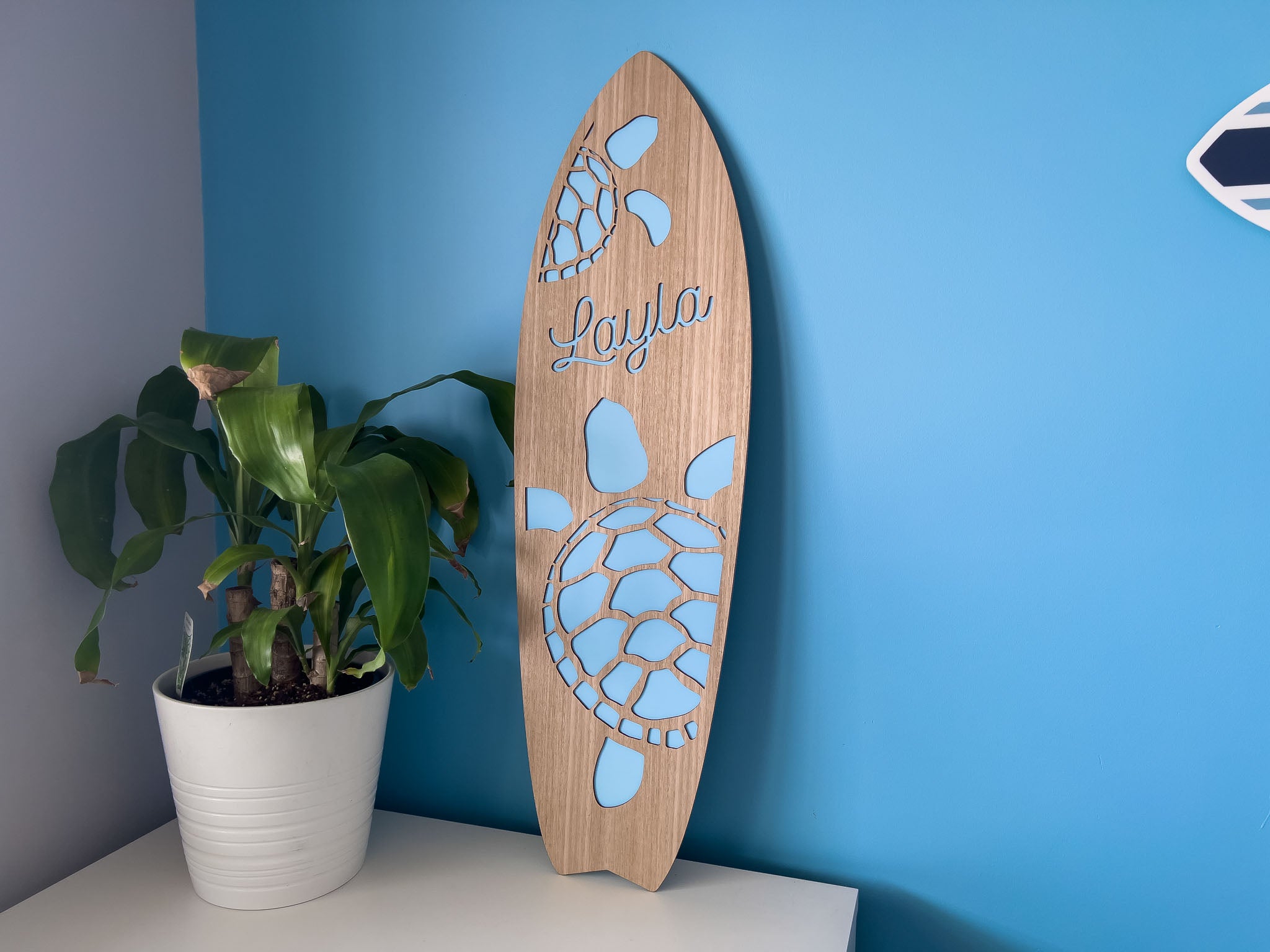 Timber surfboard name plaque in a child's bedroom that says 'Layla' with a blue background.