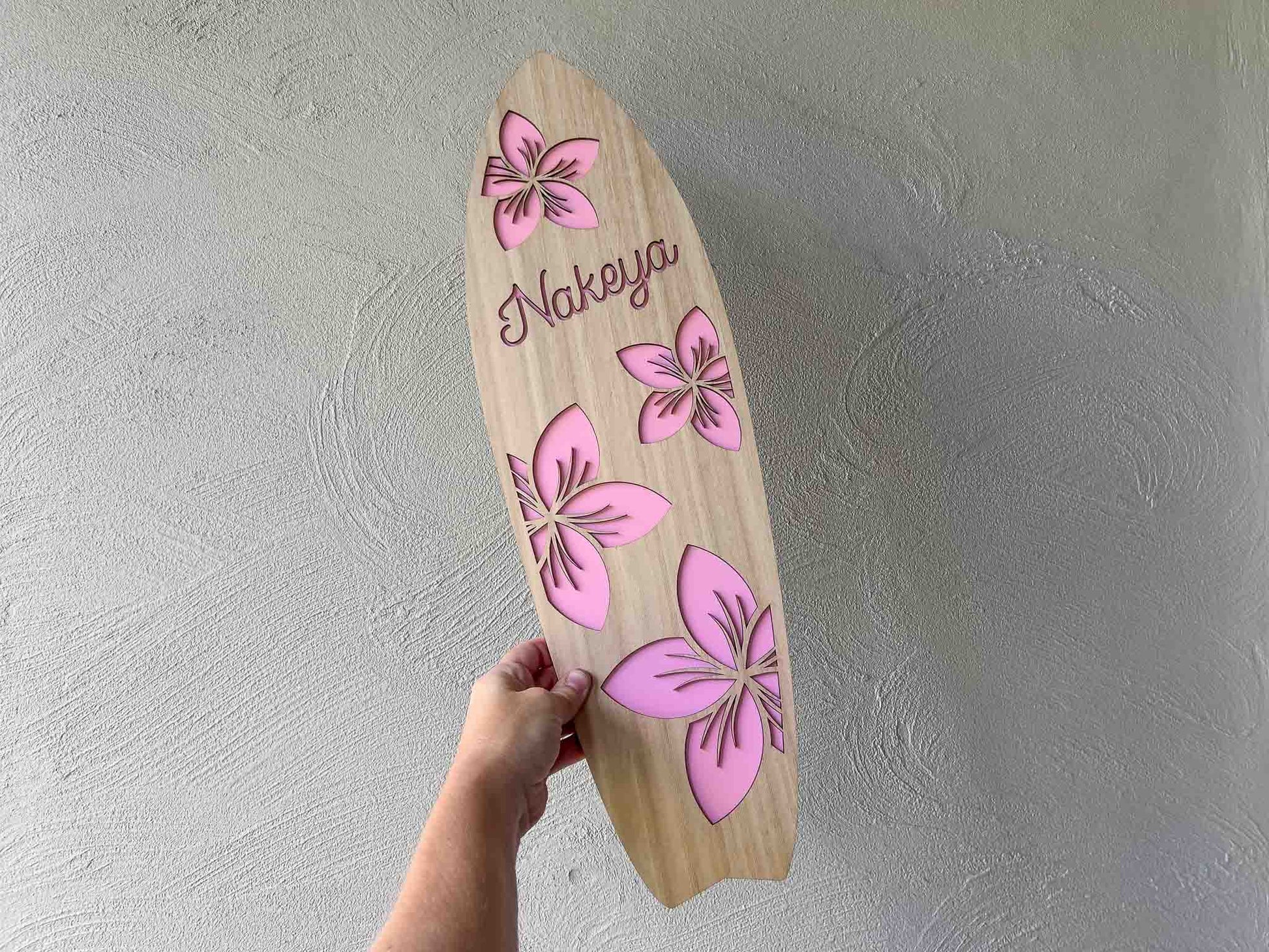 Custom made timber surfboard with pink frangipanis and the name 'Nakeya'.