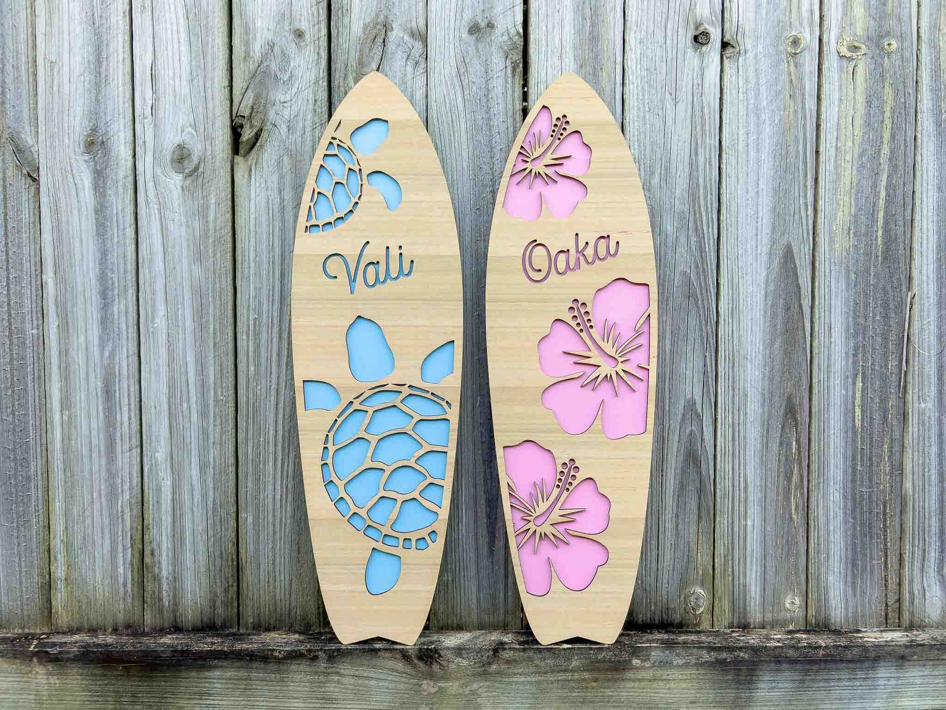 Two timber surfboards with 'Vali' in blue and 'Oaka' in pink.