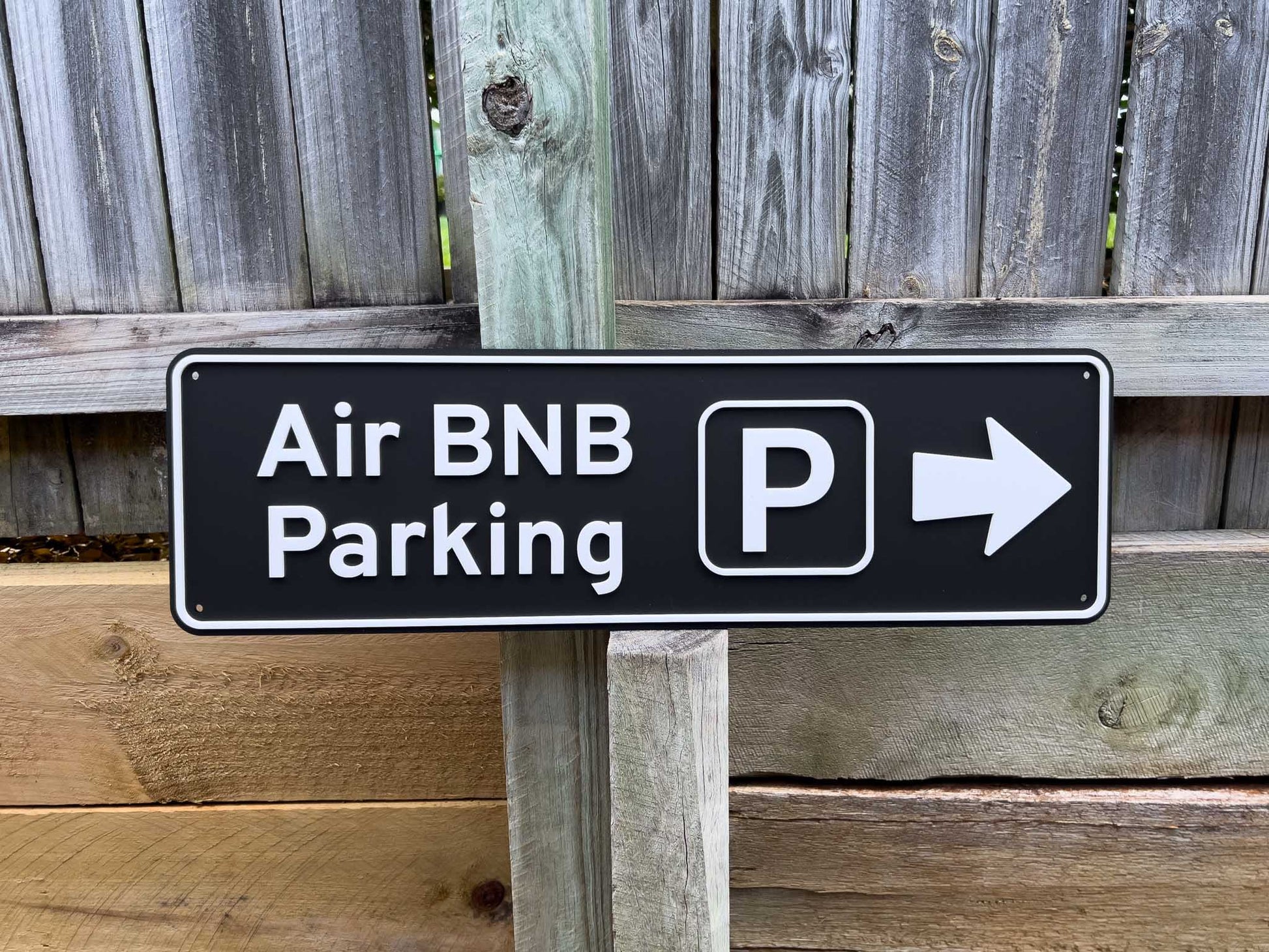 Black sign with white text and arrow indicating Air BNB Parking, mounted on a wooden post against a wooden fence | Coji Designs