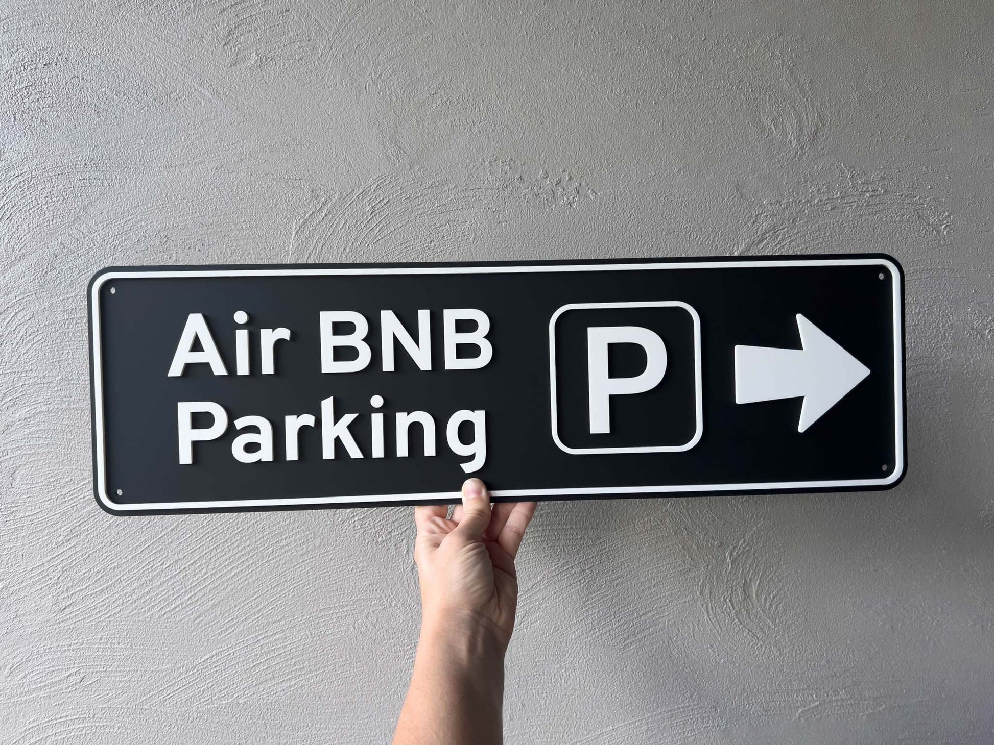 Hand holding a sign indicating Air BNB Parking with a white arrow on a gray background | Coji Designs