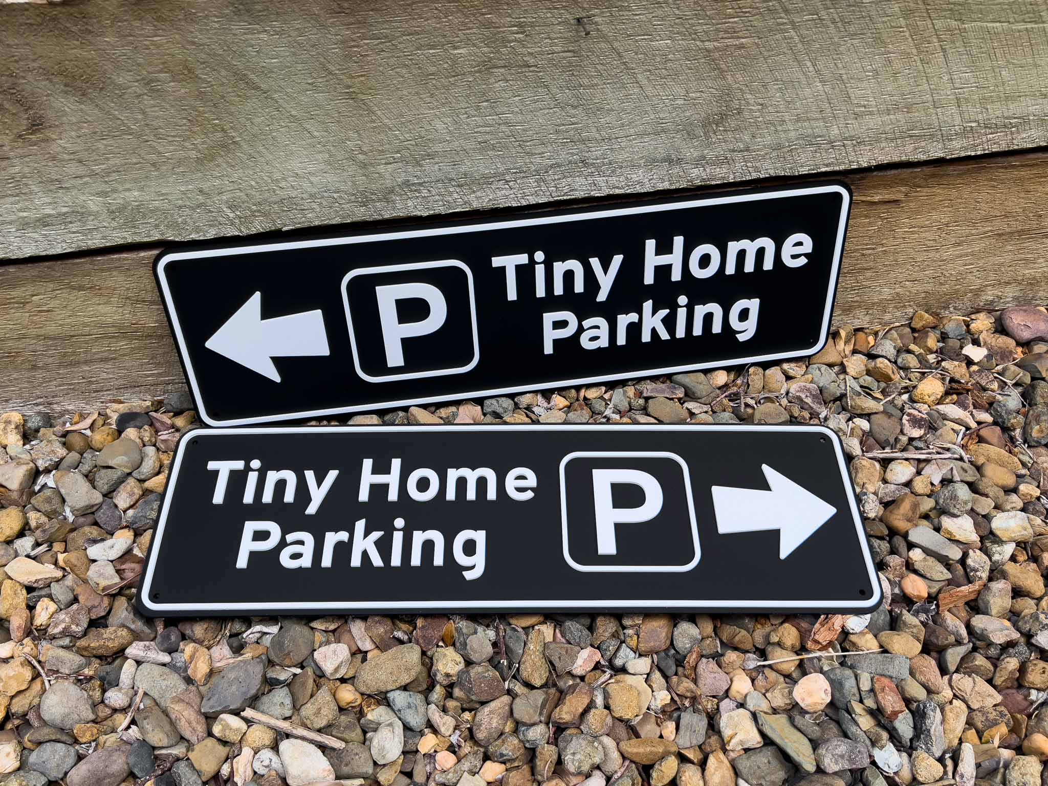 Two black signs with white text and arrows indicating 'Tiny Home Parking' on a stone surface | Coji Designs