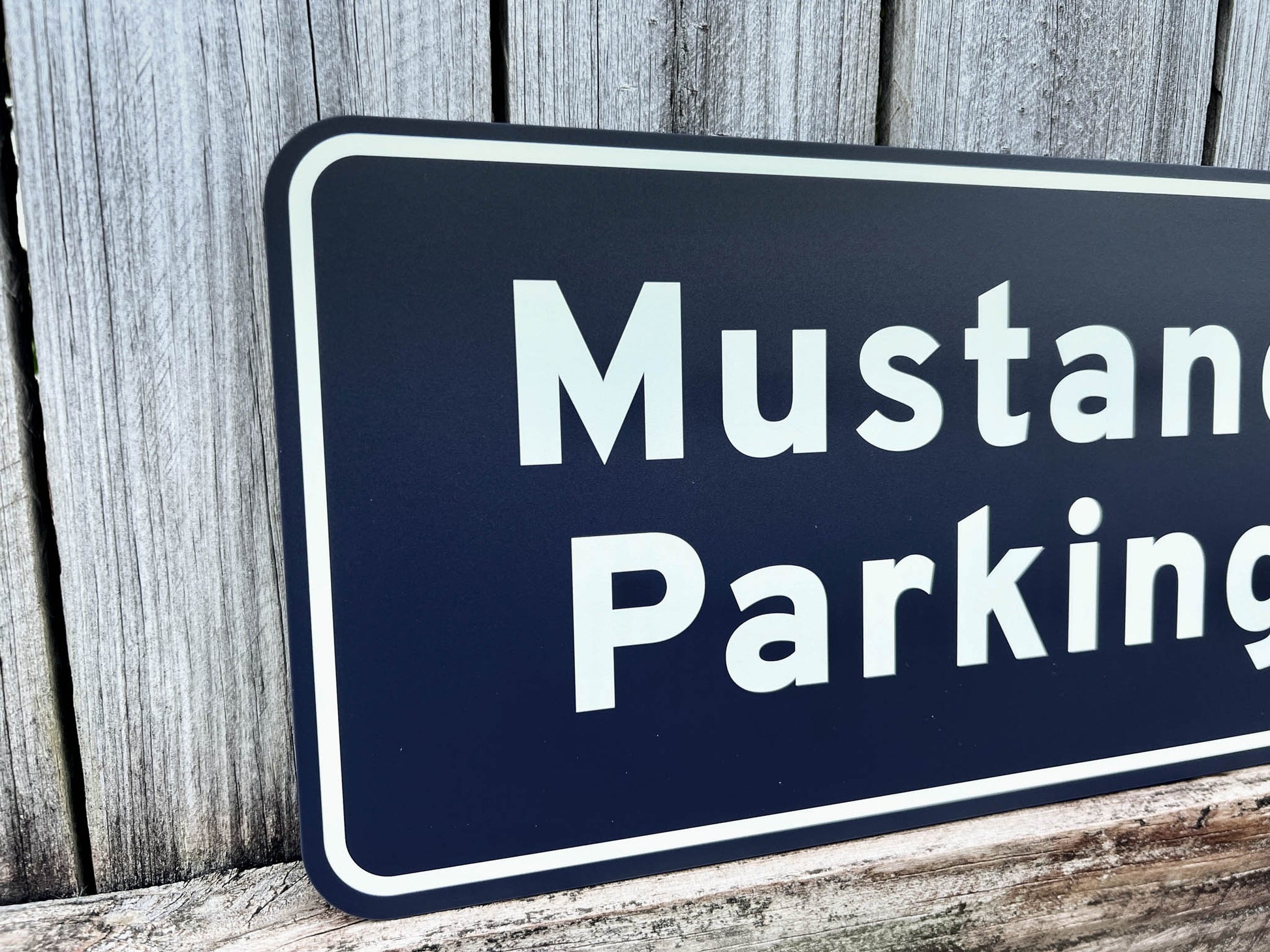Navy blue sign with white text 'Mustang Parking' against a wooden background