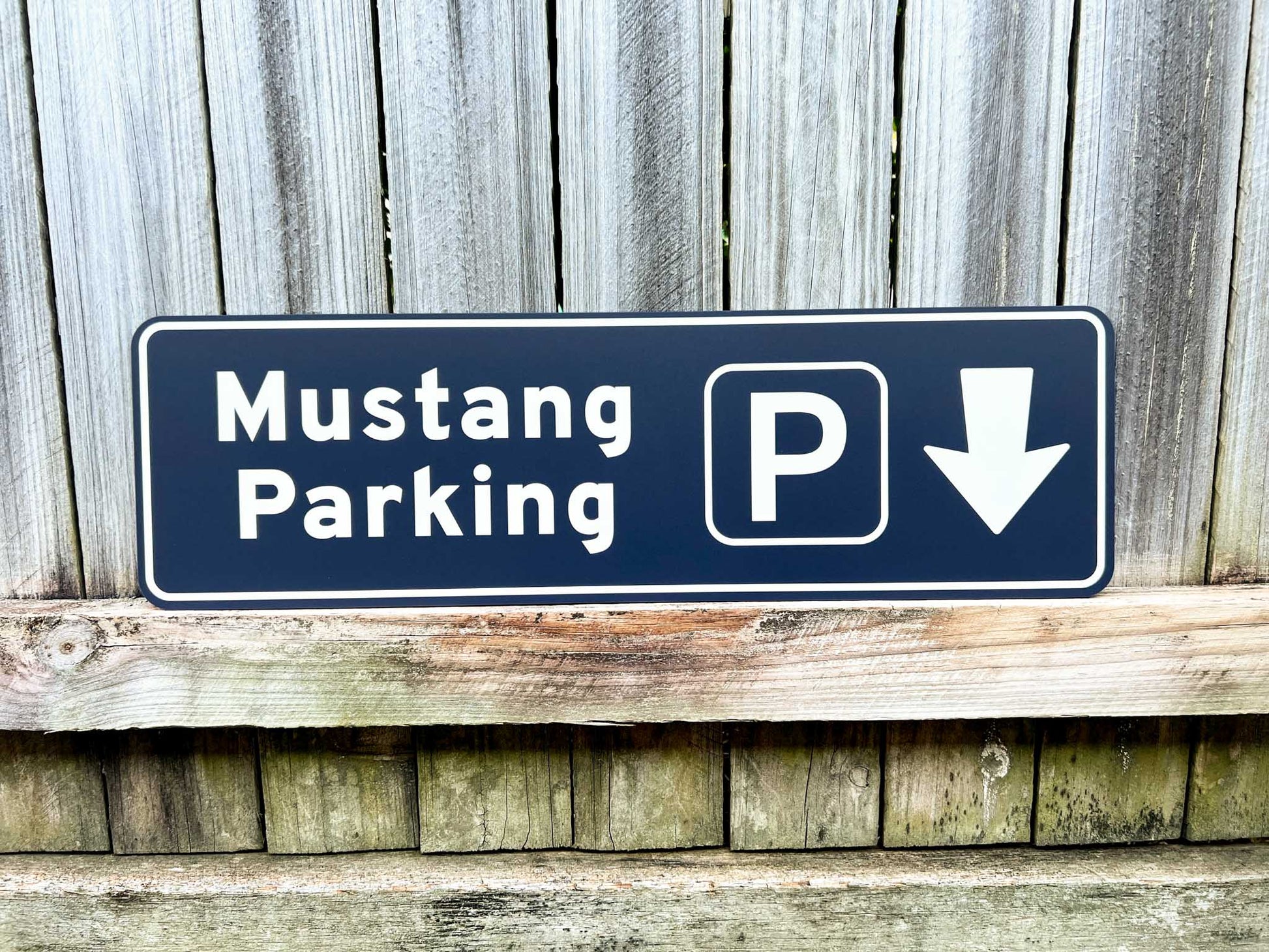 Mustang Parking sign with a white arrow pointing down on a wooden background