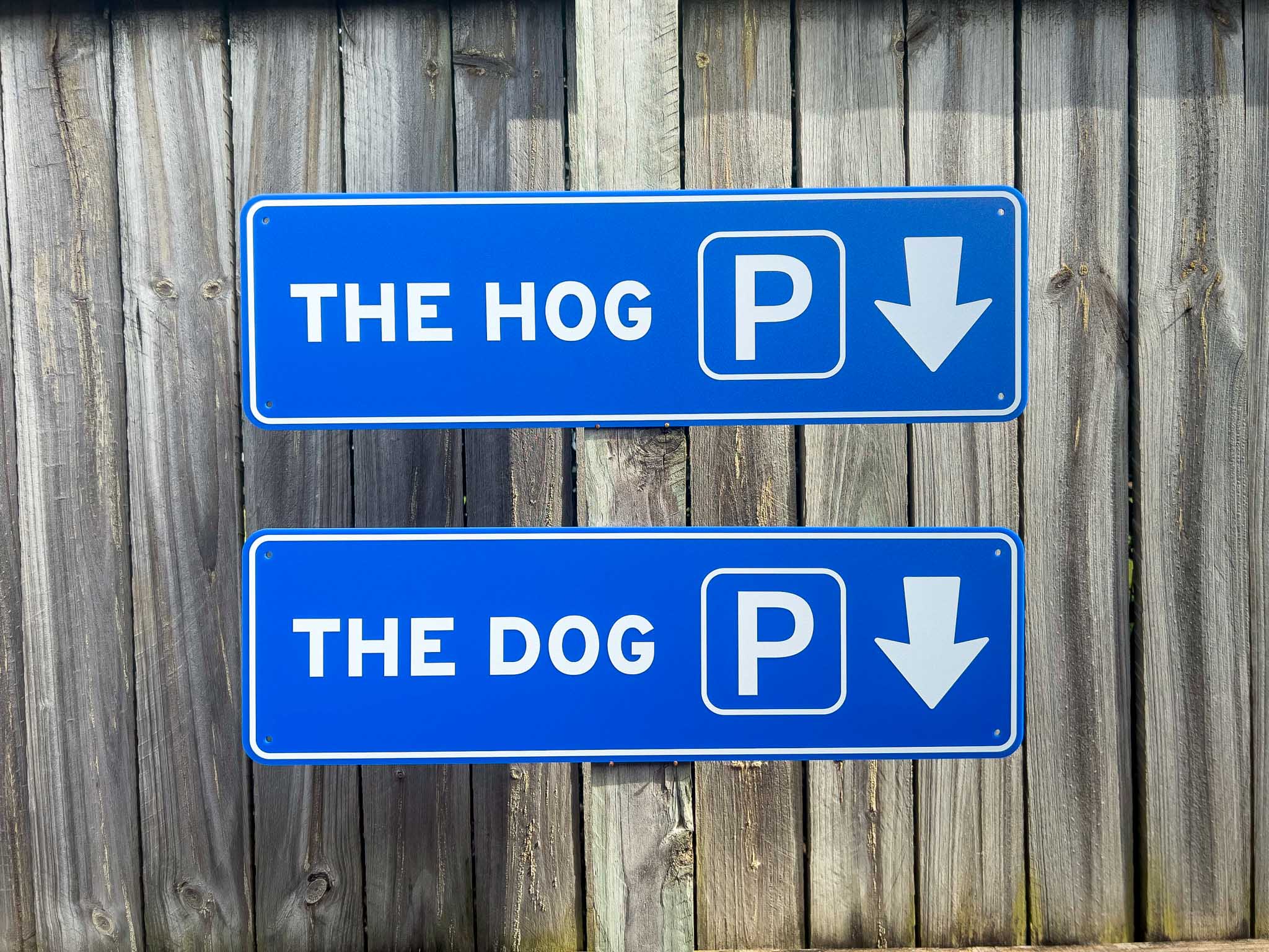 Two blue parking signs on a wooden fence, one for 'The Hog' and one for 'The Dog'.