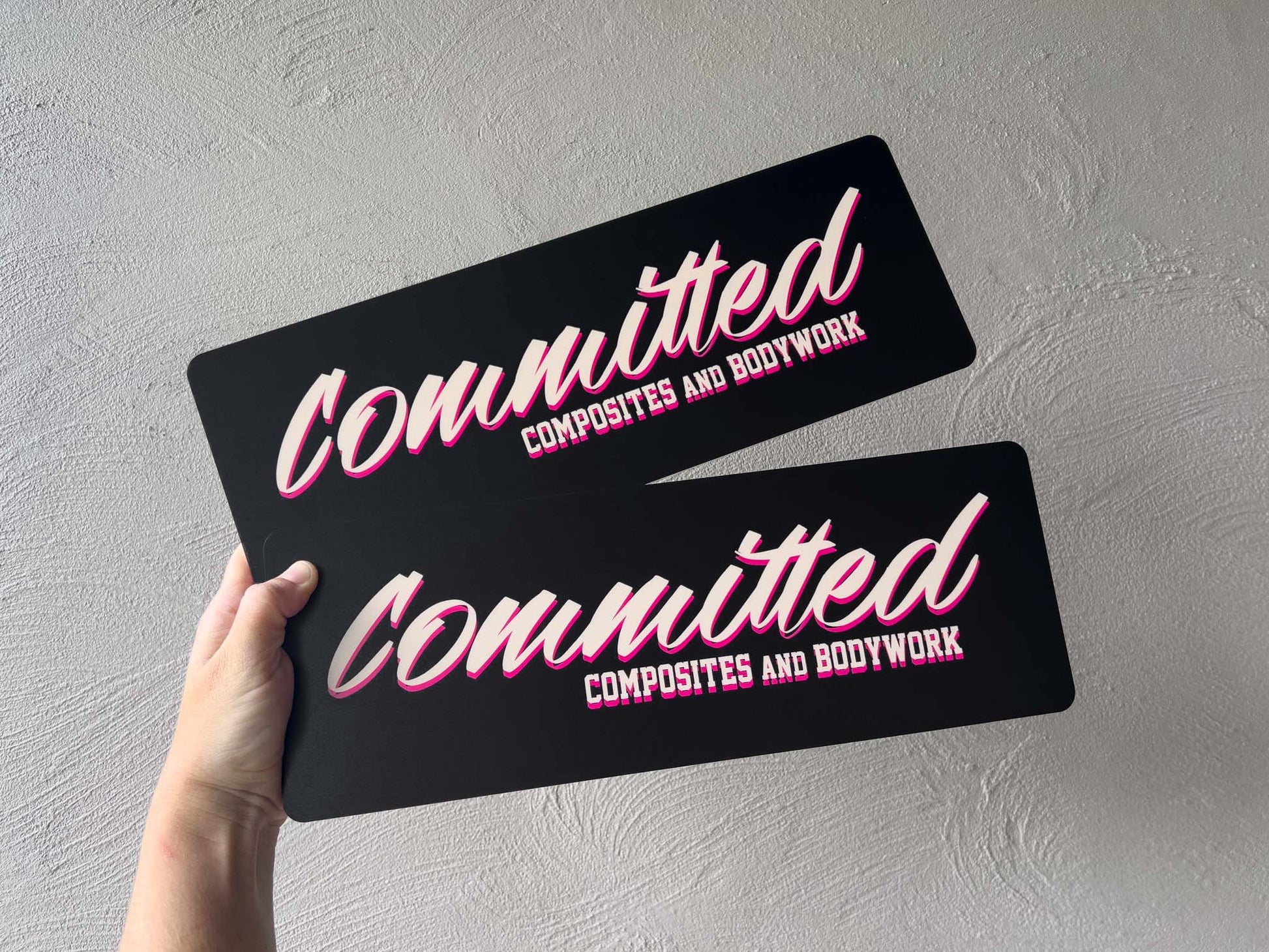 Two black UV printed acrylic plates with pink text held against a grey background