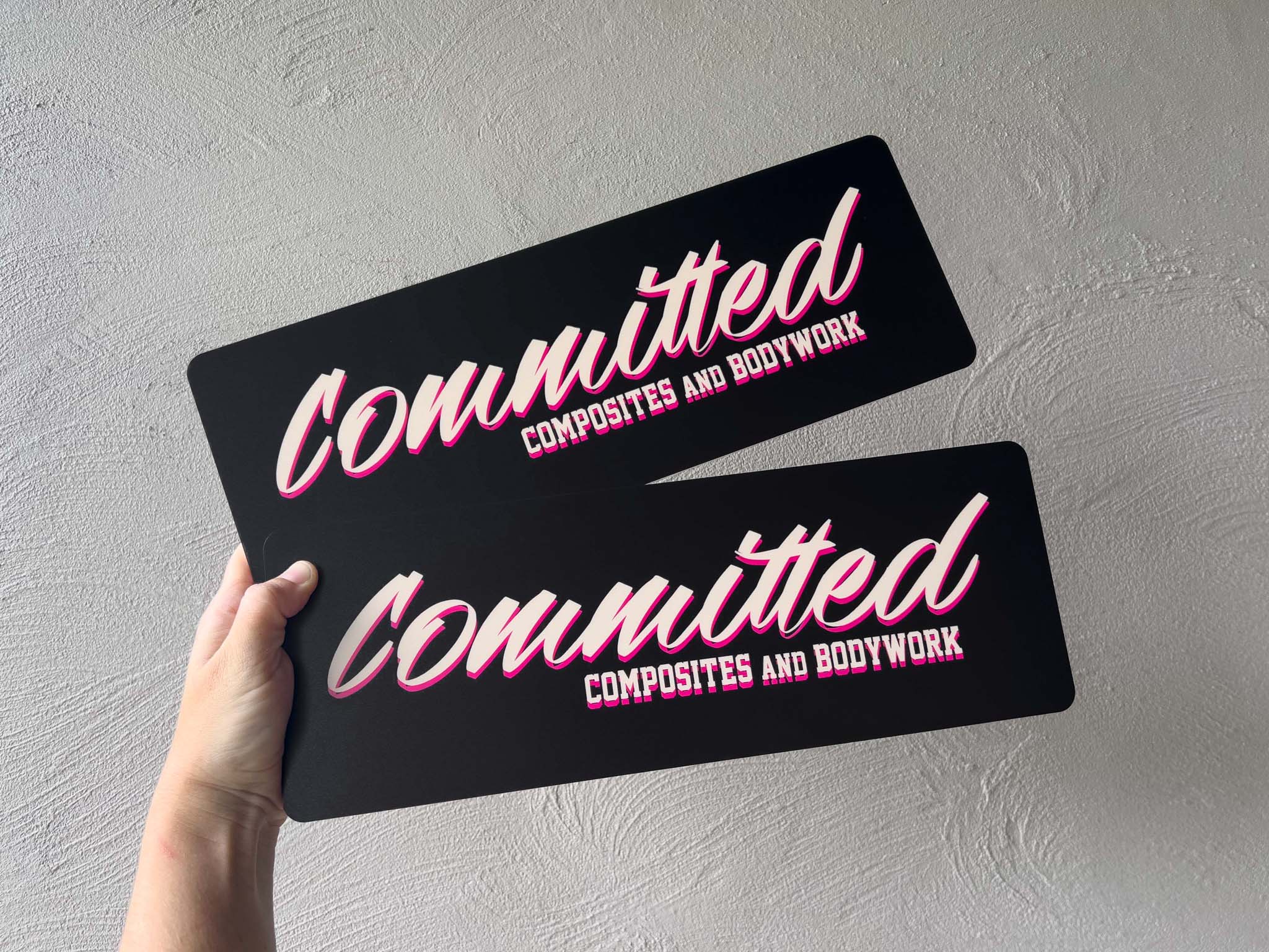 Two black UV printed acrylic plates with pink text held against a grey background