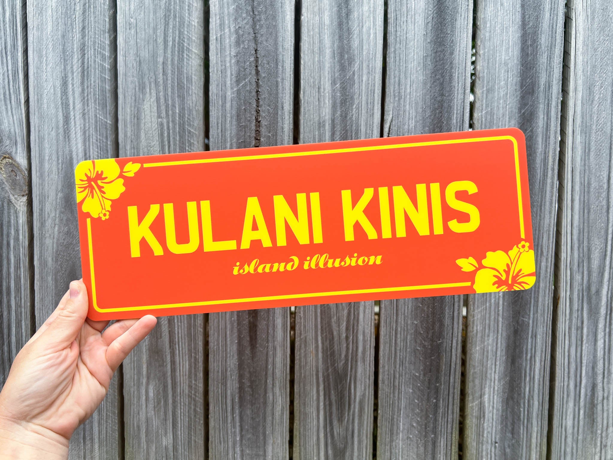 Hand holding an orange and yellow acyrlic plate with the brand name 'Kulani Kinis' on it