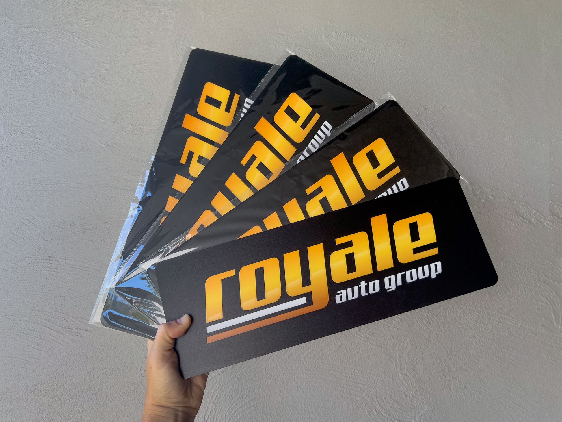 Hand holding a collection of ' Royale auto group' logo plate signs against a plain background