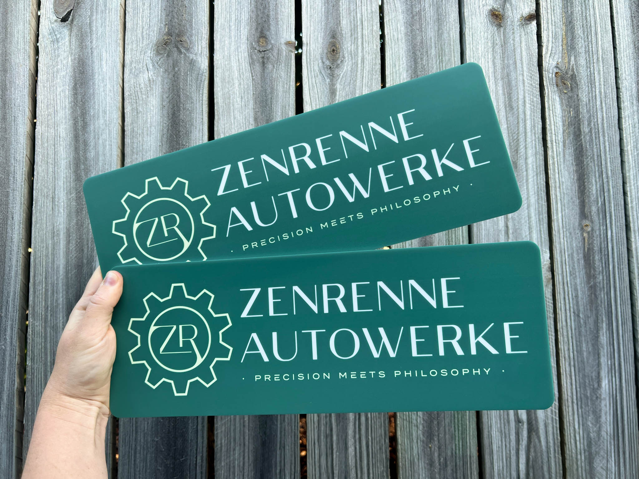 Two green dispaly signs with 'Zenrenne Autowerke' branding held against a wooden background.