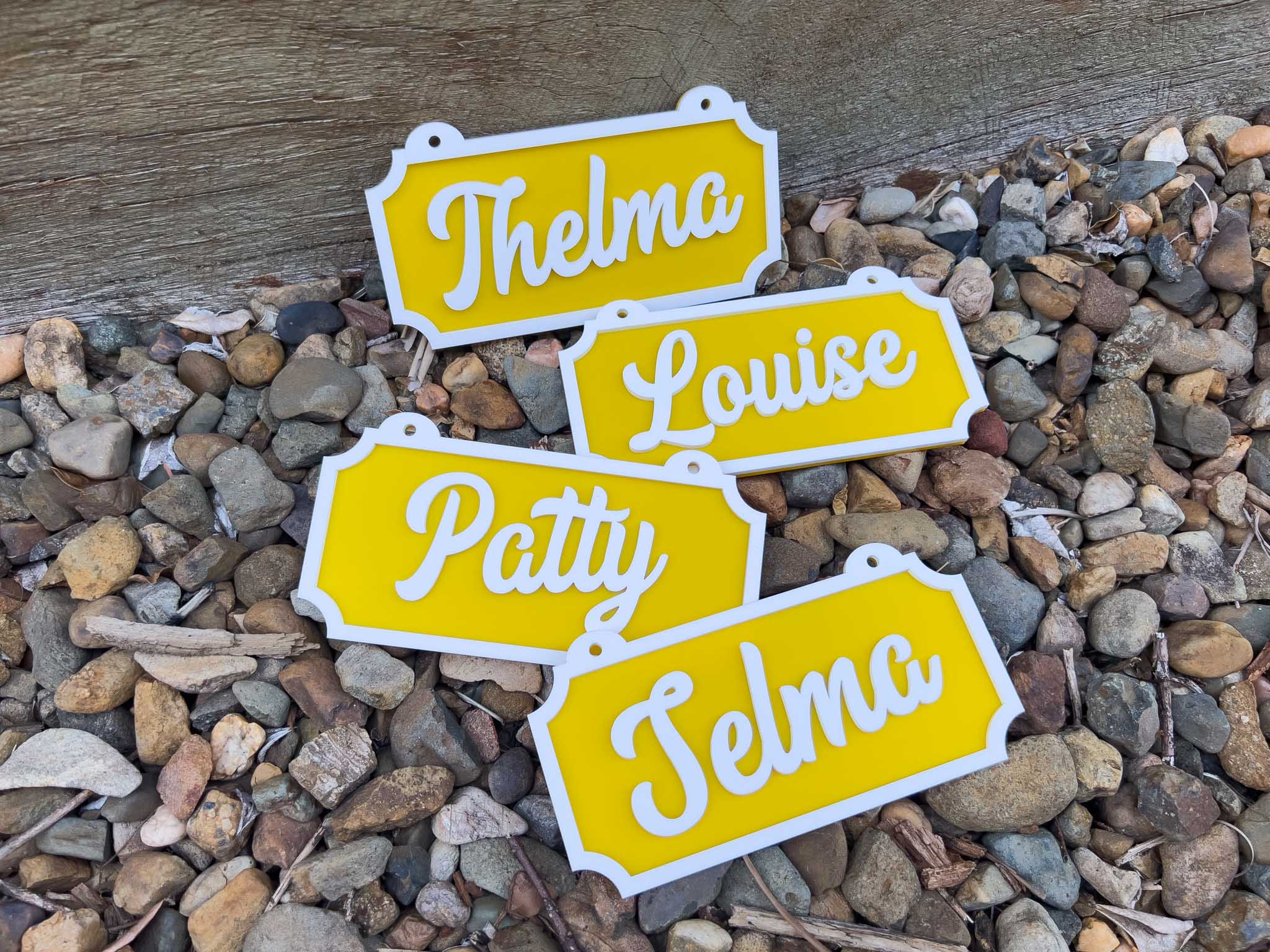 Four yellow nameplates with white text on a bed of small stones | Coji Designs
