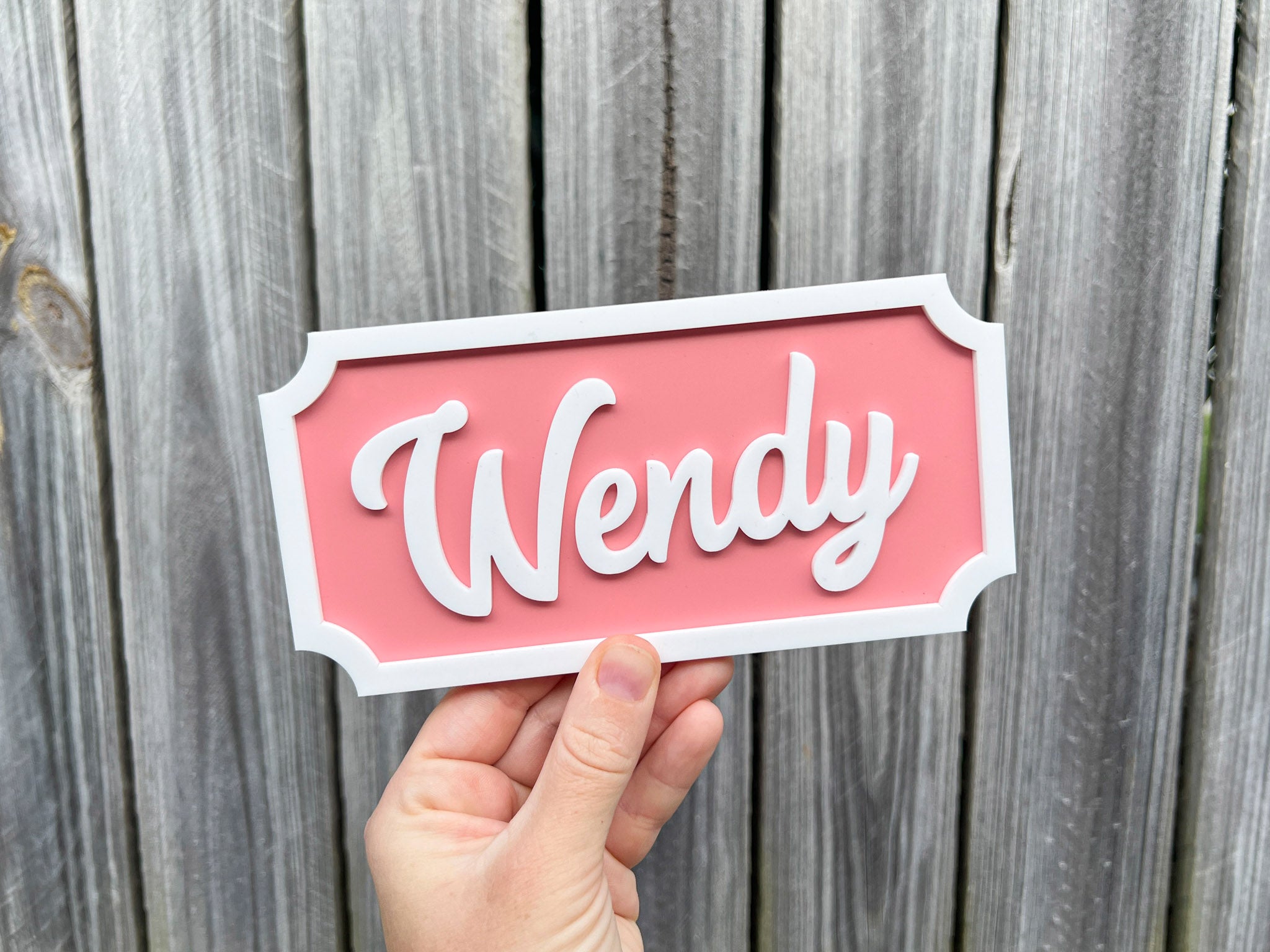 Hand holding a pink sign with 'Wendy' on a wooden background | Coji Designs