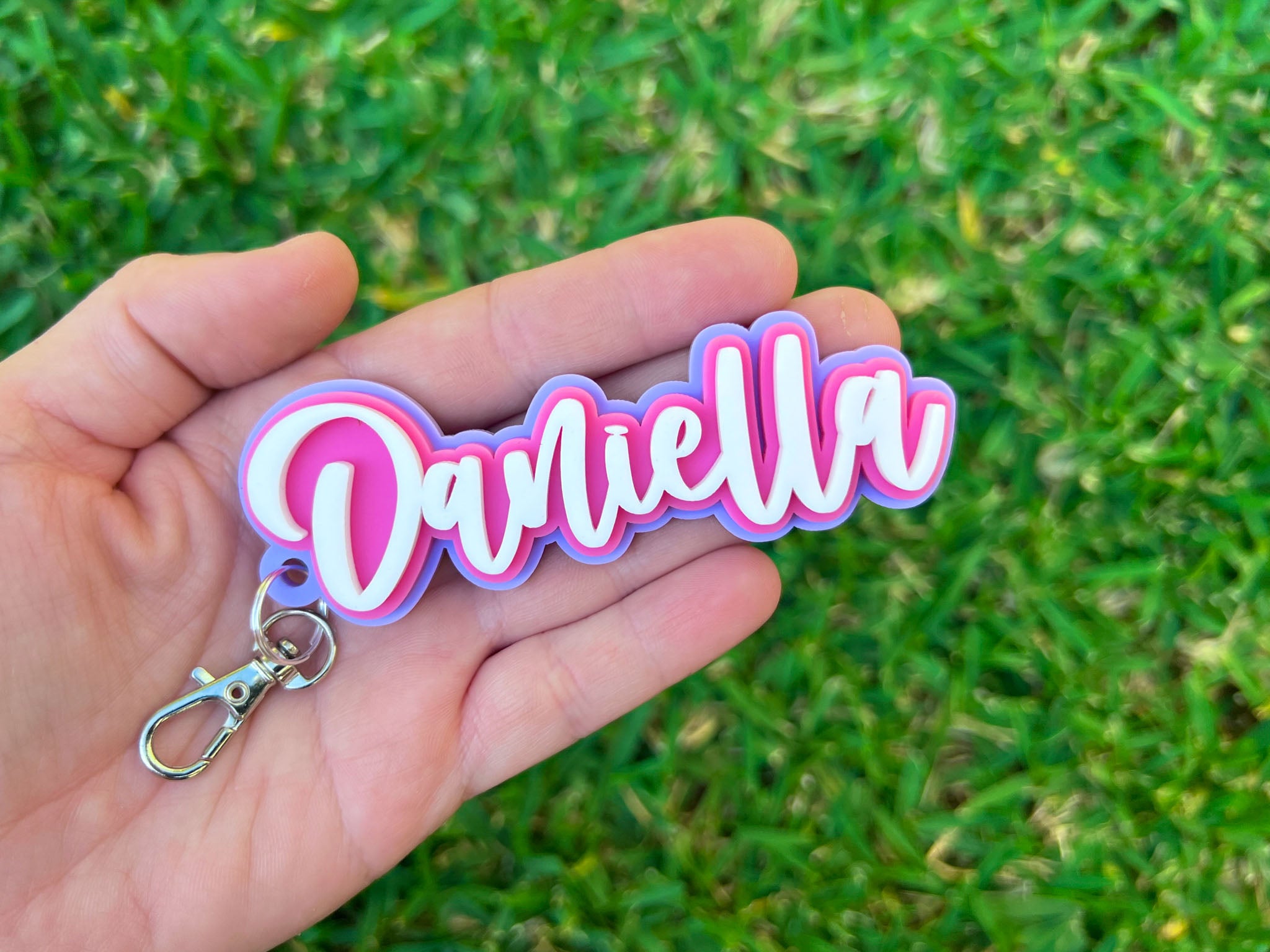 A surfy style 3D acrylic keychain in pink, purple and white with the name 'Daniella'.