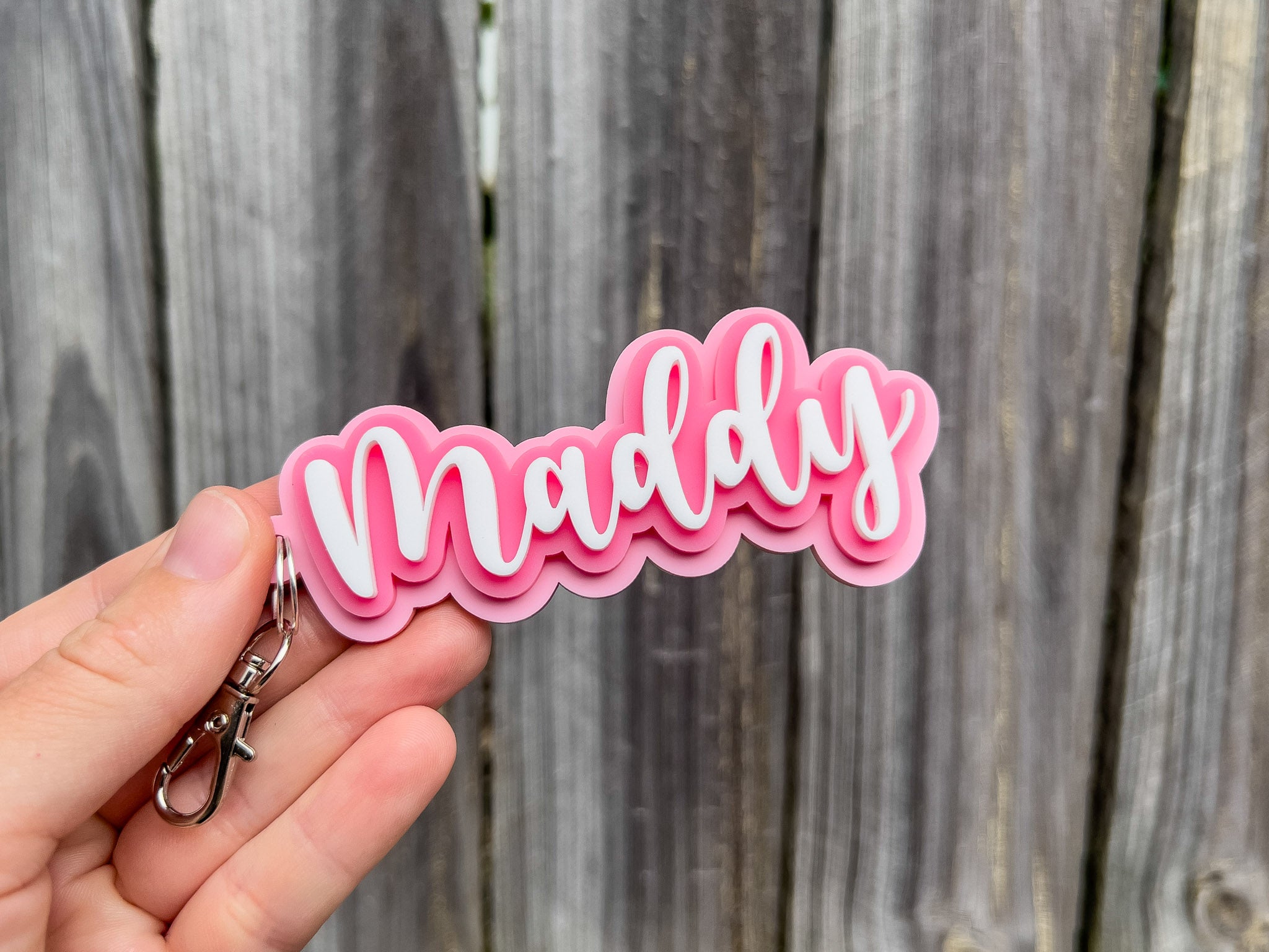 A cute pink and white 3D acrylic name tag keychain with a handwritten script font that reads 'Maddy'