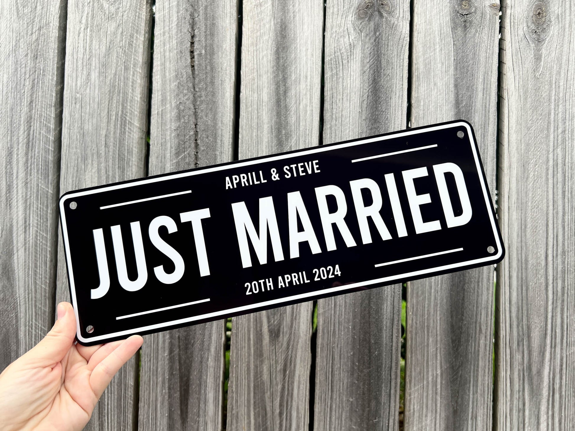 Street sign with 'Just Married' text held by a hand against a wooden fence background | Coji Designs