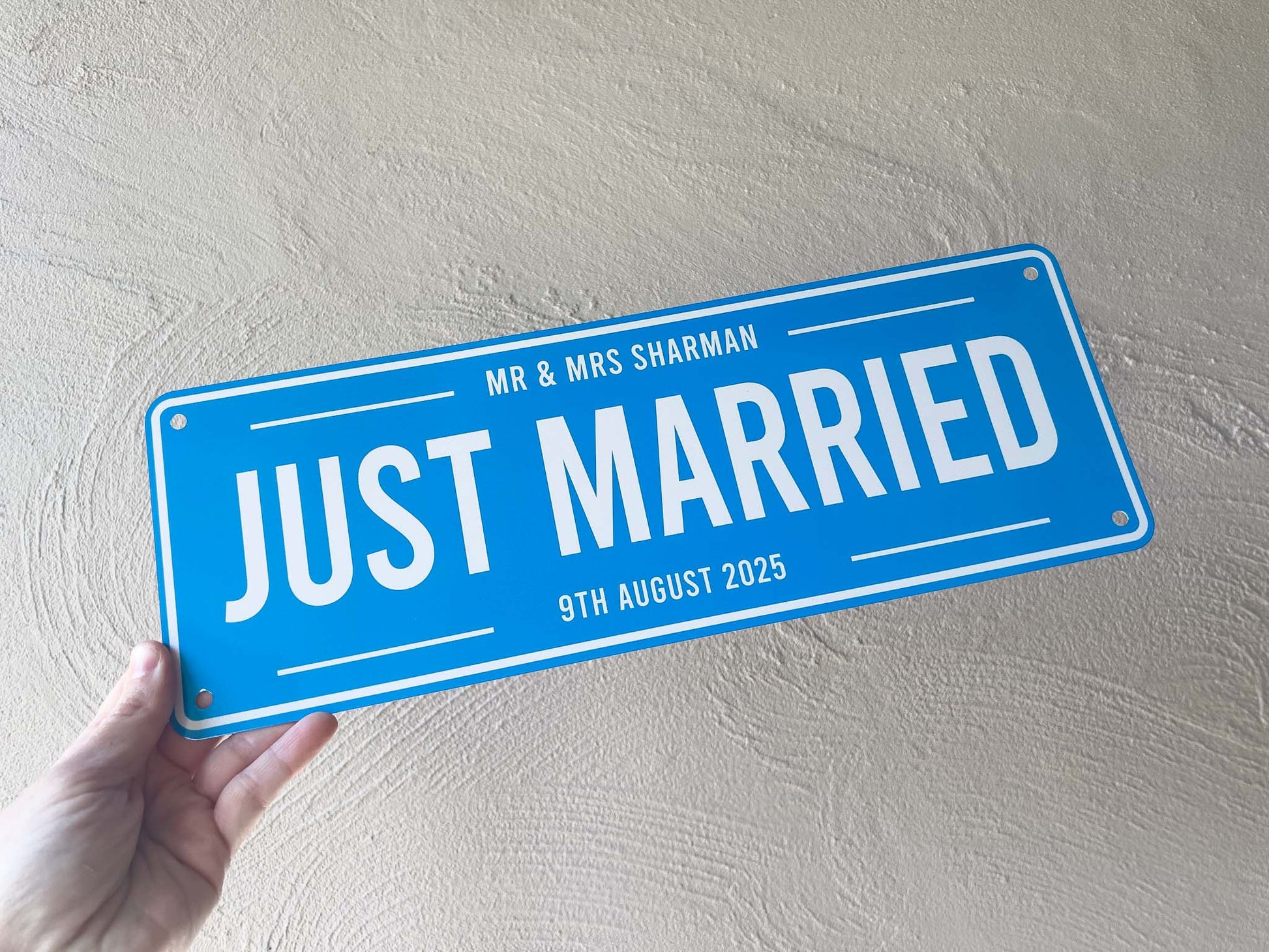 Blue sign with 'Just Married' text held against a light gray wall | Coji Designs