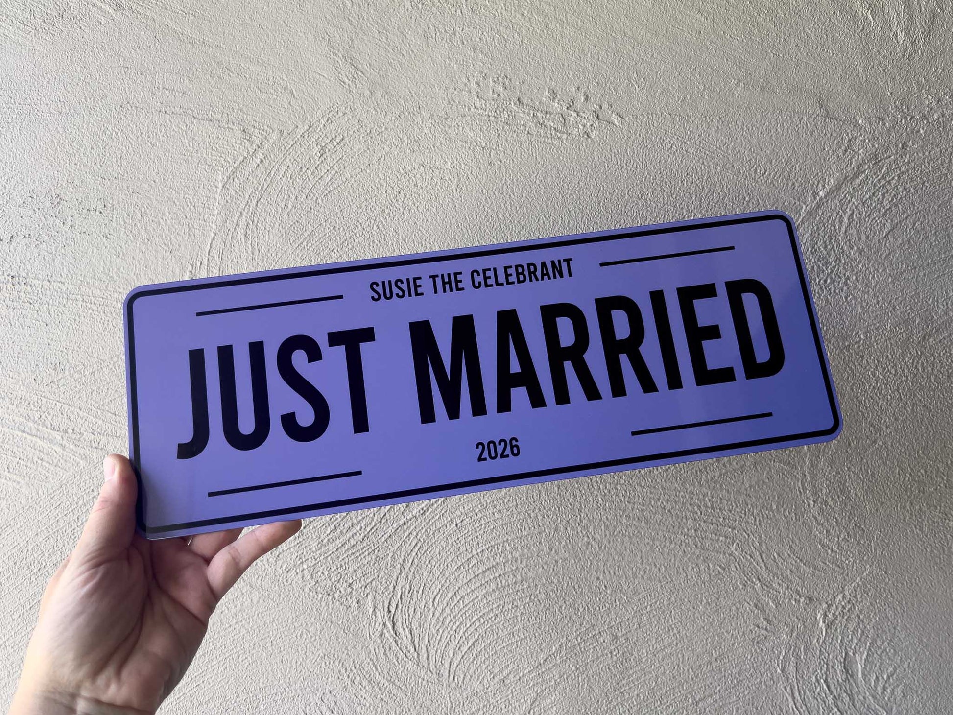 Hand holding a 'Just Married' sign with personalized text against a light gray background | Coji Designs