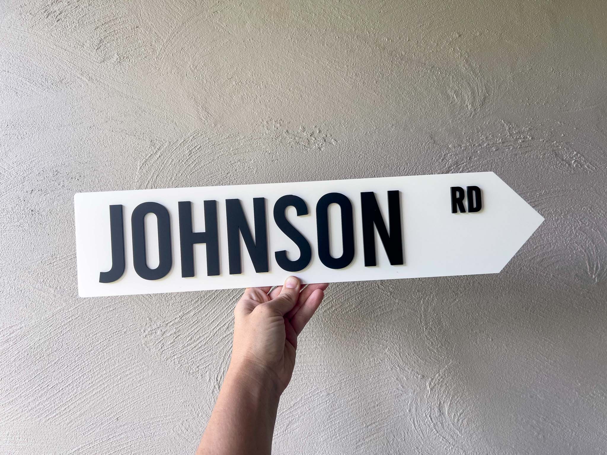 Hand holding a white sign with 'JOHNSON RD' on a plain background | Coji Designs
