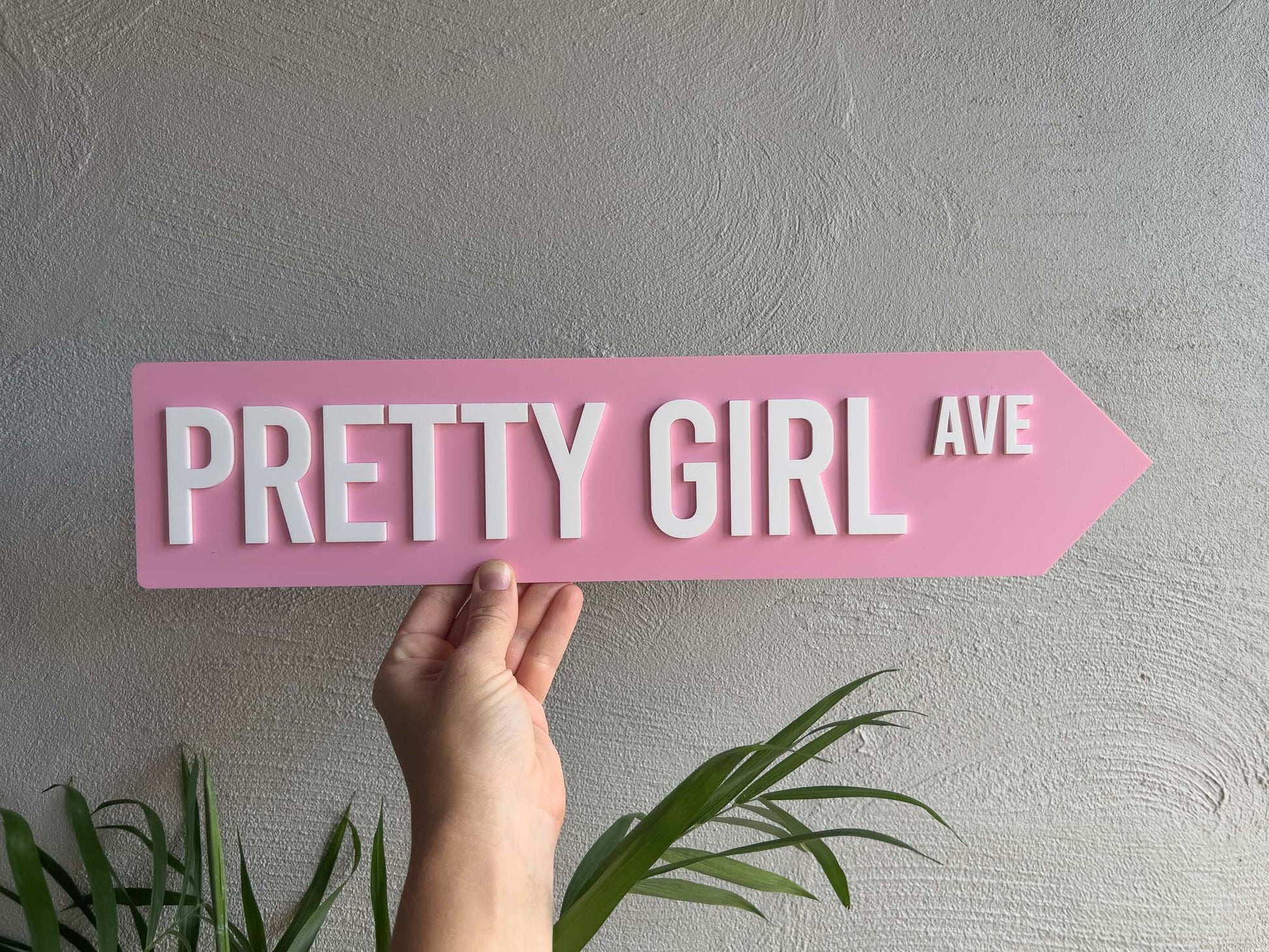 Hand holding a pink sign with 'Pretty Girl Ave' text against a gray wall | Coji Designs