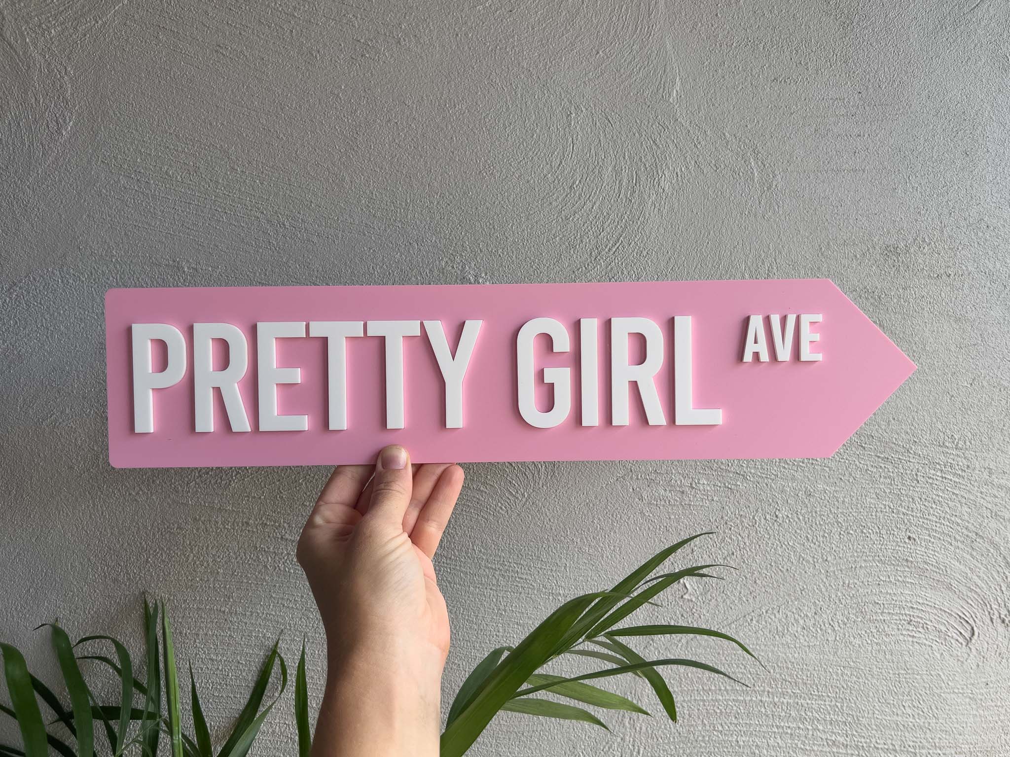 Hand holding a pink sign with 'Pretty Girl Ave' text against a gray wall | Coji Designs