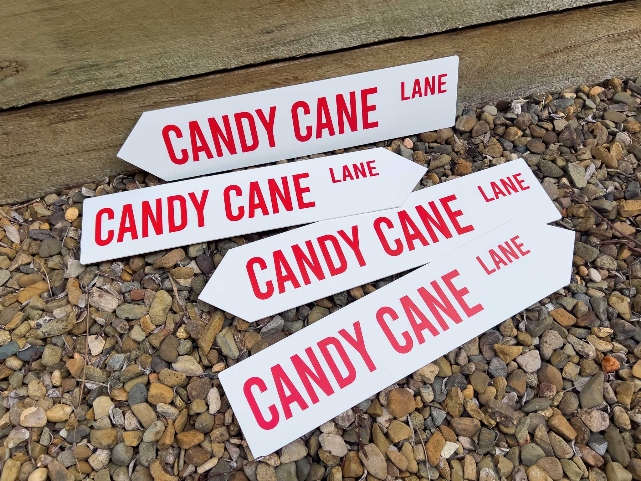Four white signs with red text reading 'CANDY CANE LANE' on a gravel surface.