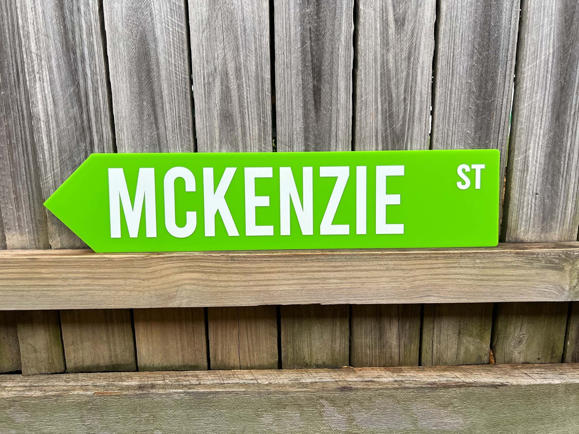 Green street sign with 'MCKENZIE ST' text on a wooden surface