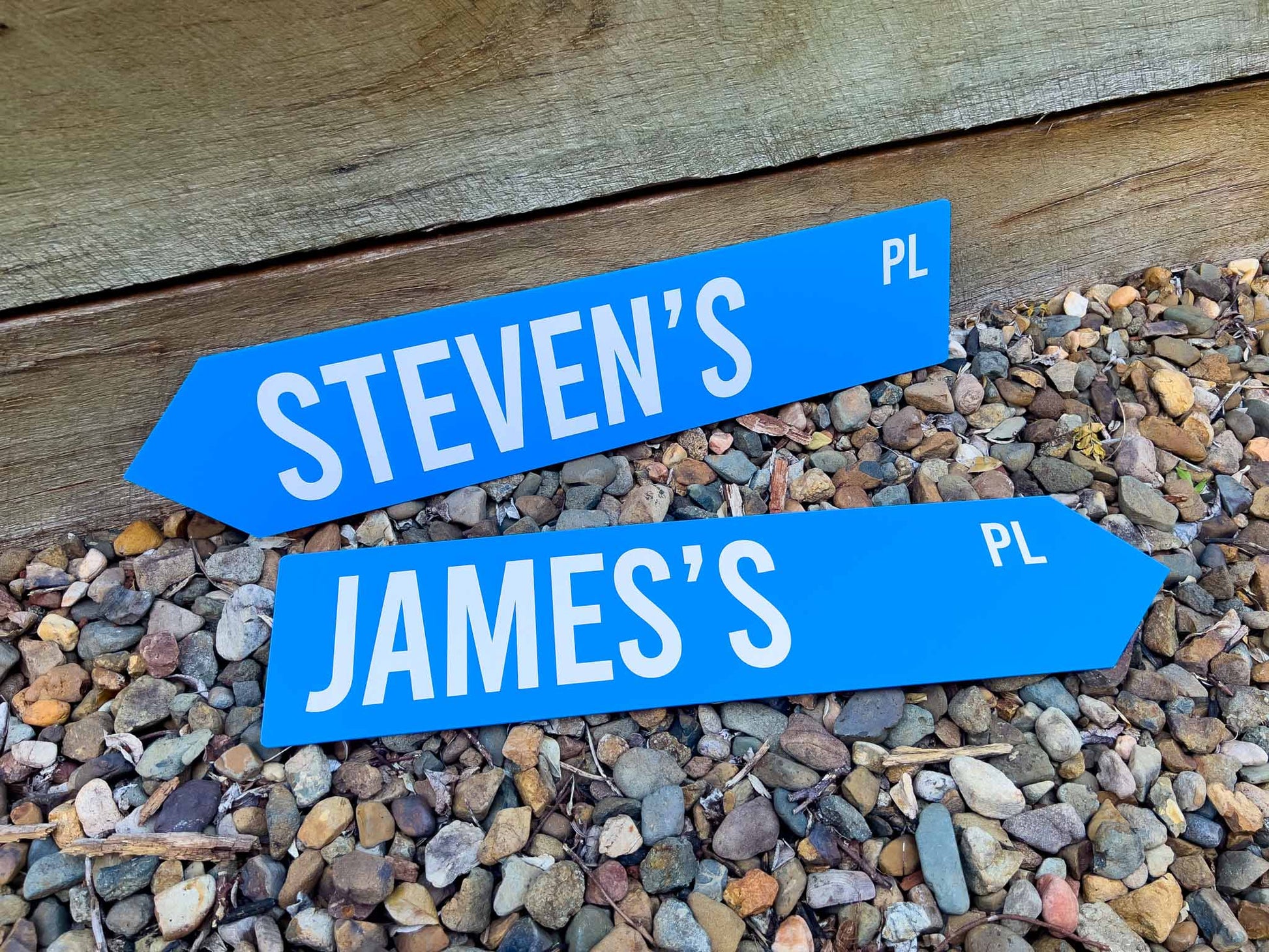 Two blue arrow-shaped signs with 'STEVEN'S PL' and 'JAMES'S PL' on a pebbly surface.