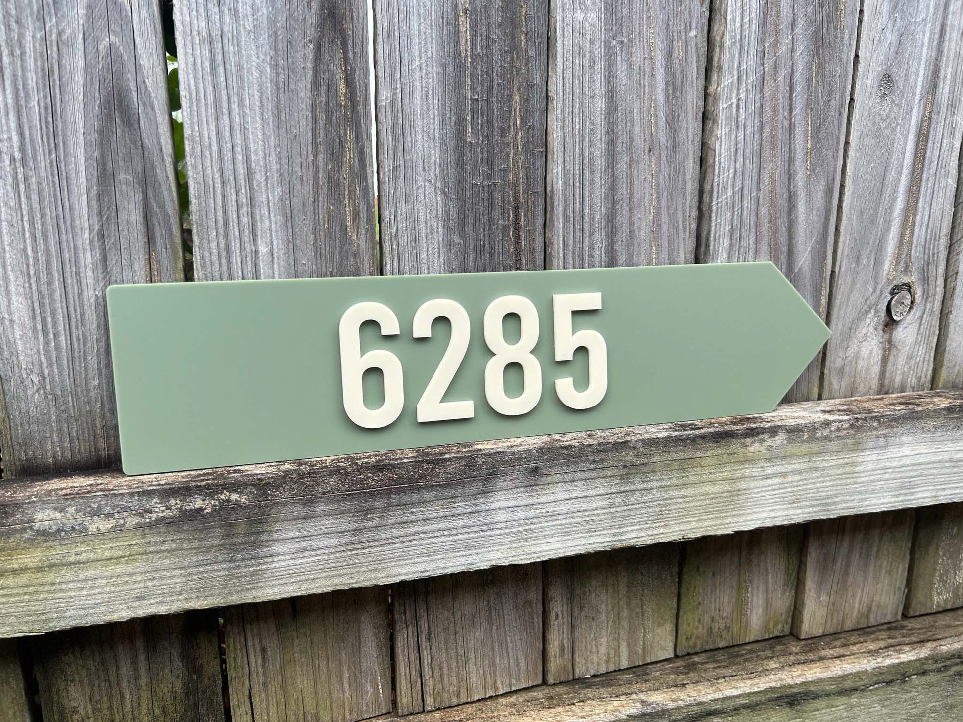 Green arrow-shaped house number sign with '6285' on a wooden background | Coji Designs
