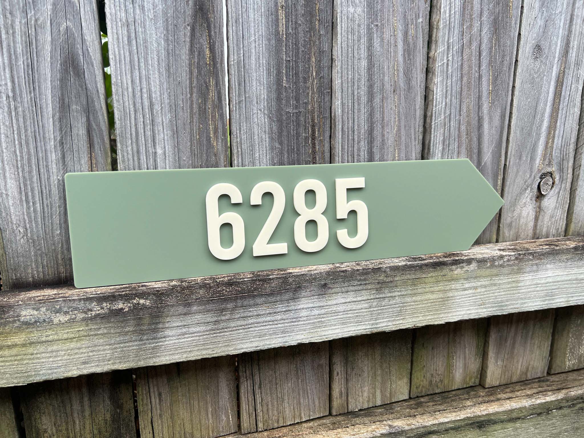 Green arrow-shaped house number sign with '6285' on a wooden background | Coji Designs