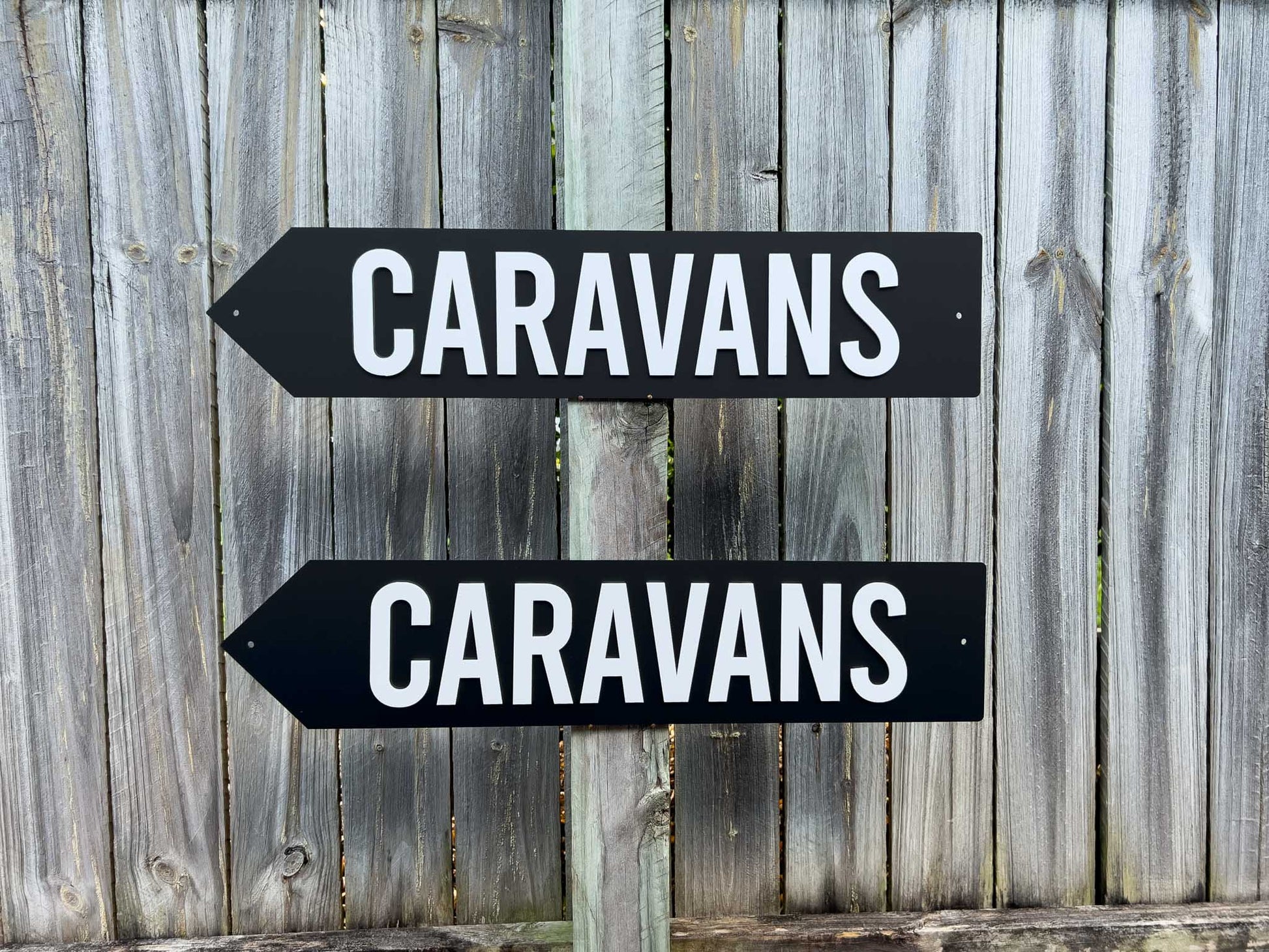 Two black and white signs pointing to 'Caravans' on a wooden fence background | Coji Designs