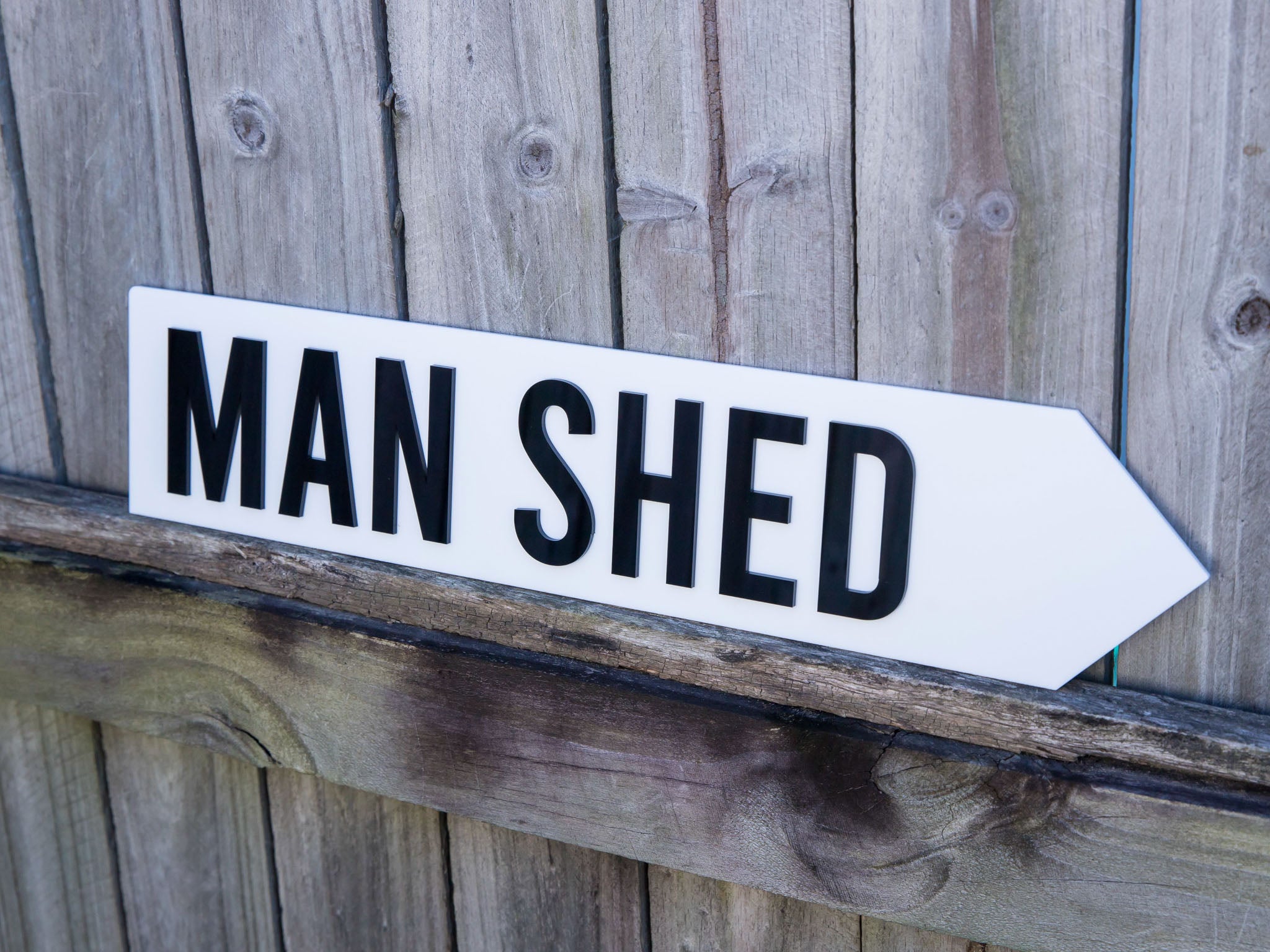 White arrow-shaped sign with 'MAN SHED' text on a wooden background | Coji Designs
