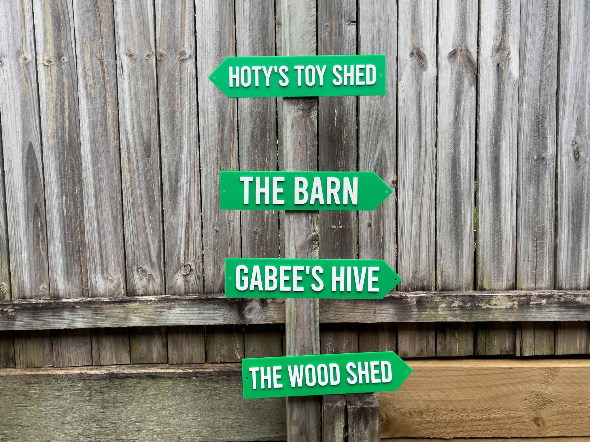 Set of green signs indicating different areas on a wooden fence | Coji Designs