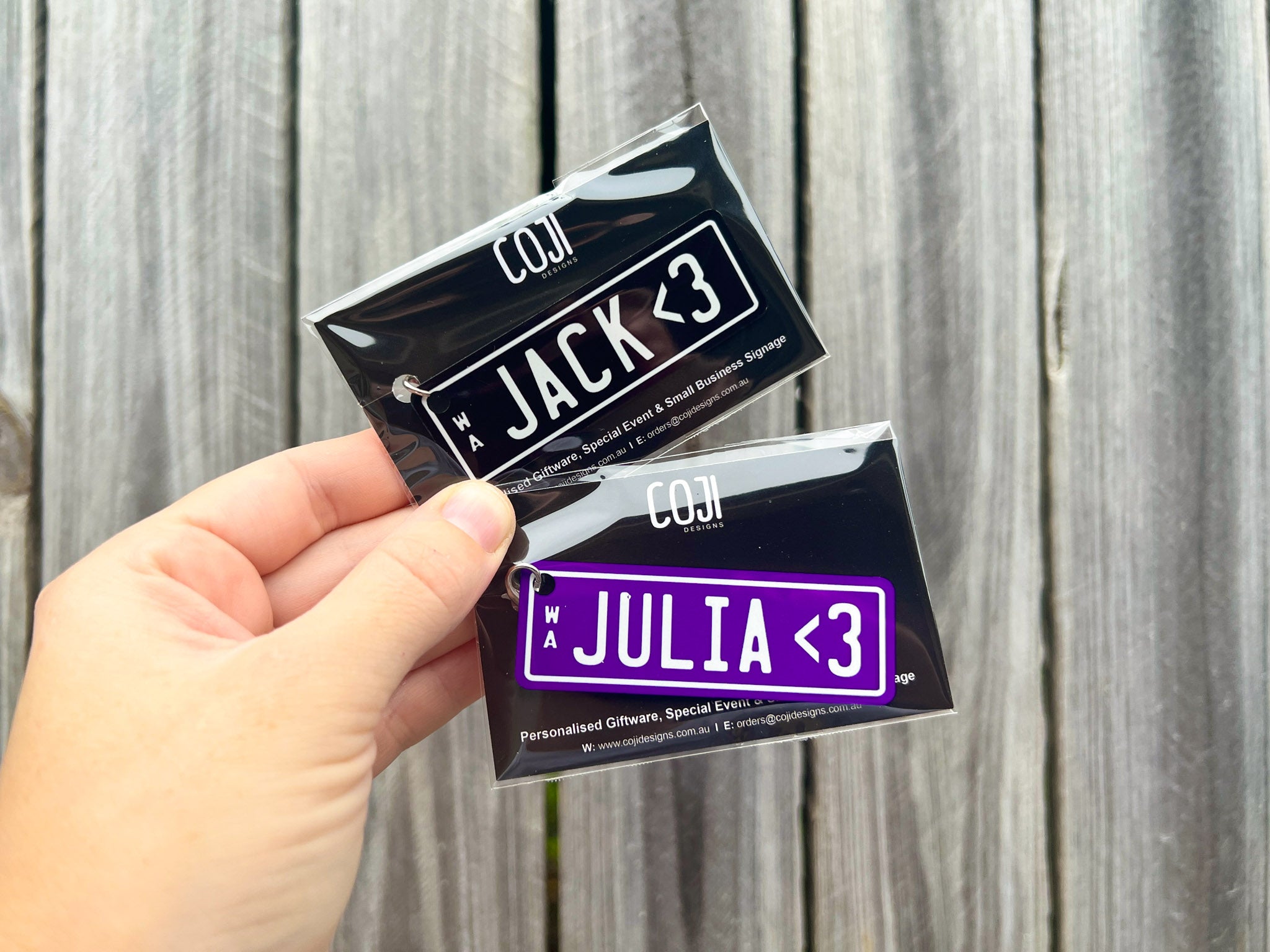 Two personalized stickers with names 'JACK' and 'JULIA' held against a wooden background.