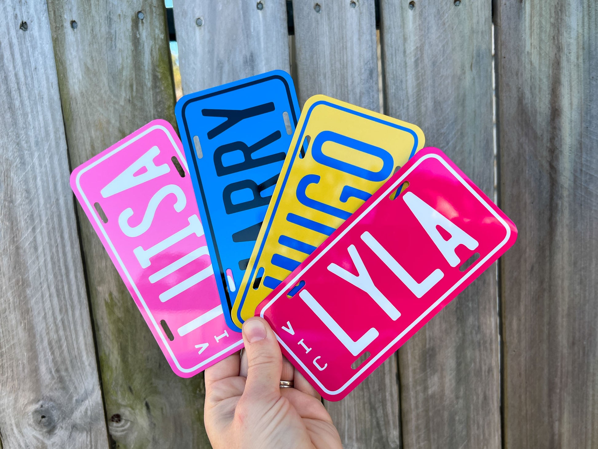 Four colorful license plate-style name plates held against a wooden background