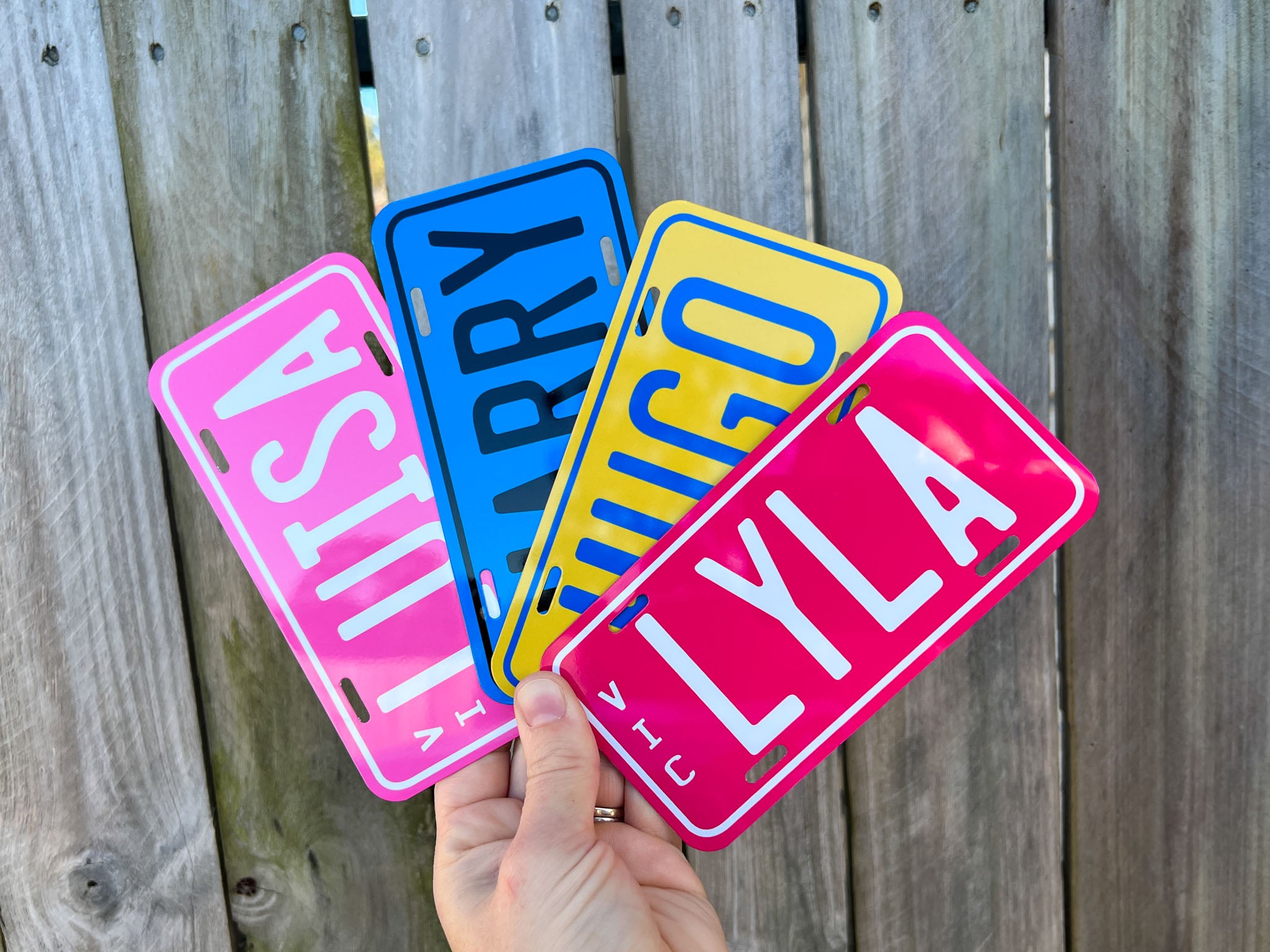 Four colorful license plate-style name plates held against a wooden background