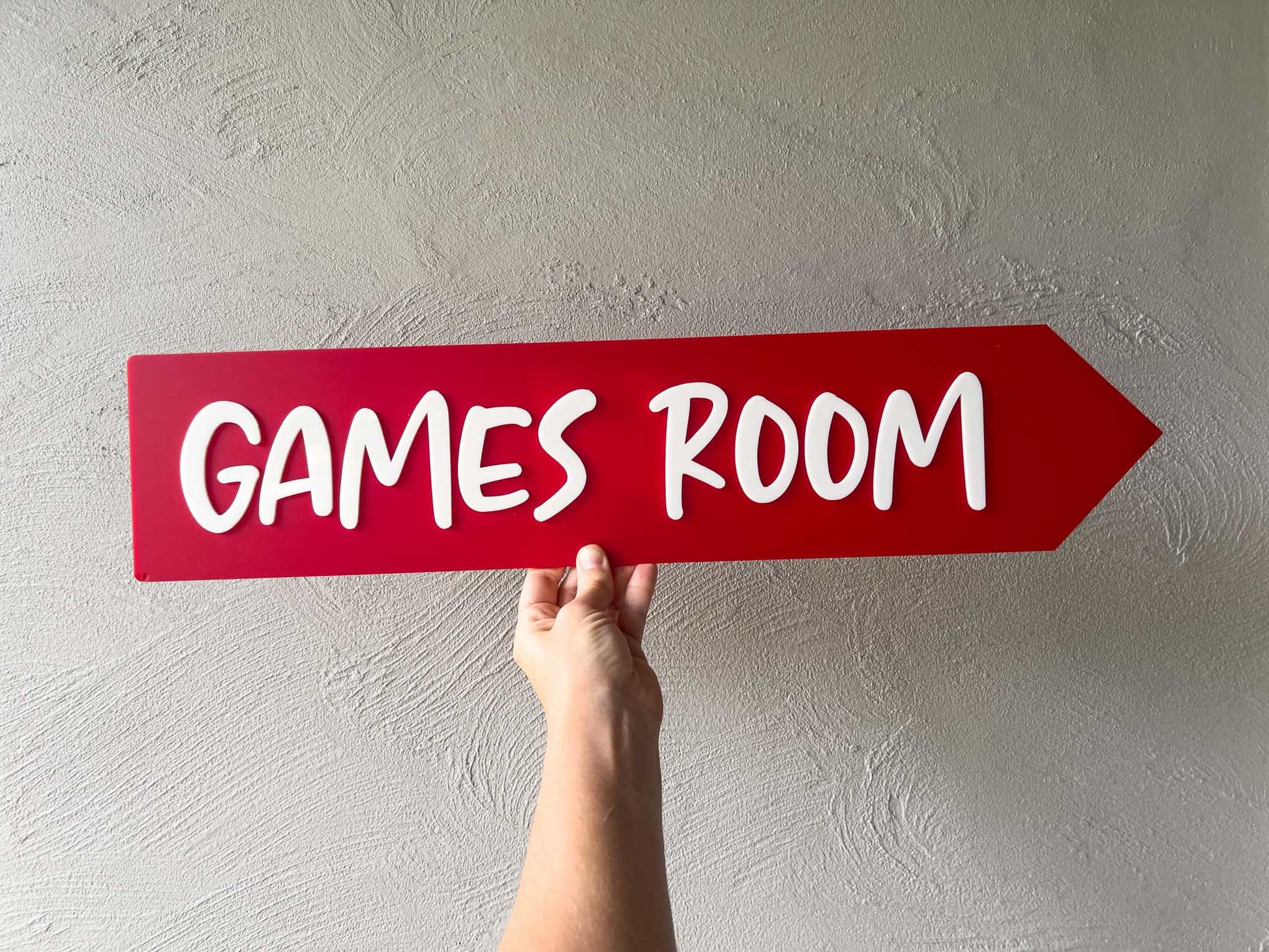 Hand holding a red sign with 'GAMES ROOM' text against a light gray wall | Coji Designs