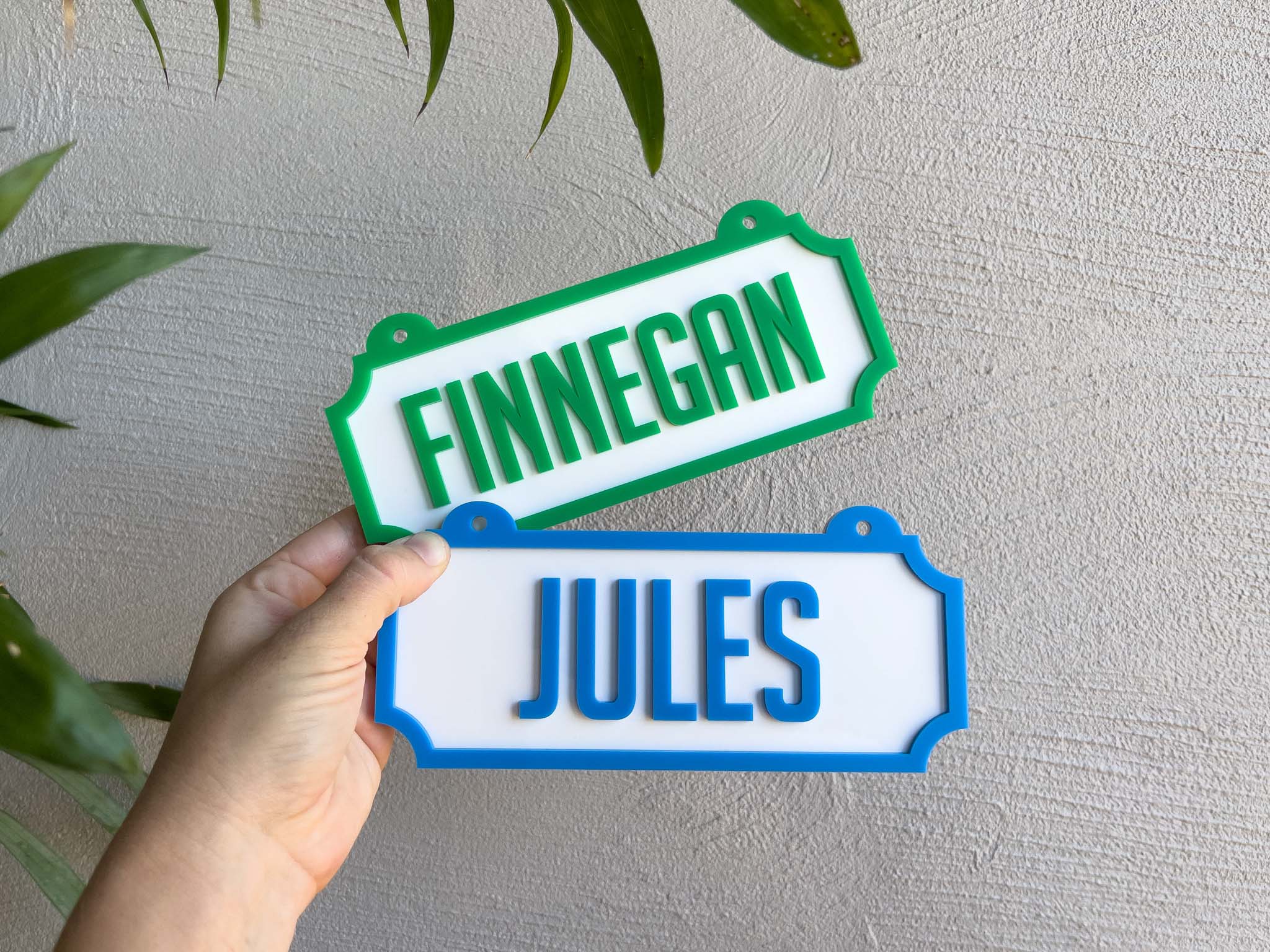 Two name plates with 'FINNEGAN' and 'JULES' text held against a light grey wall  | Coji Designs