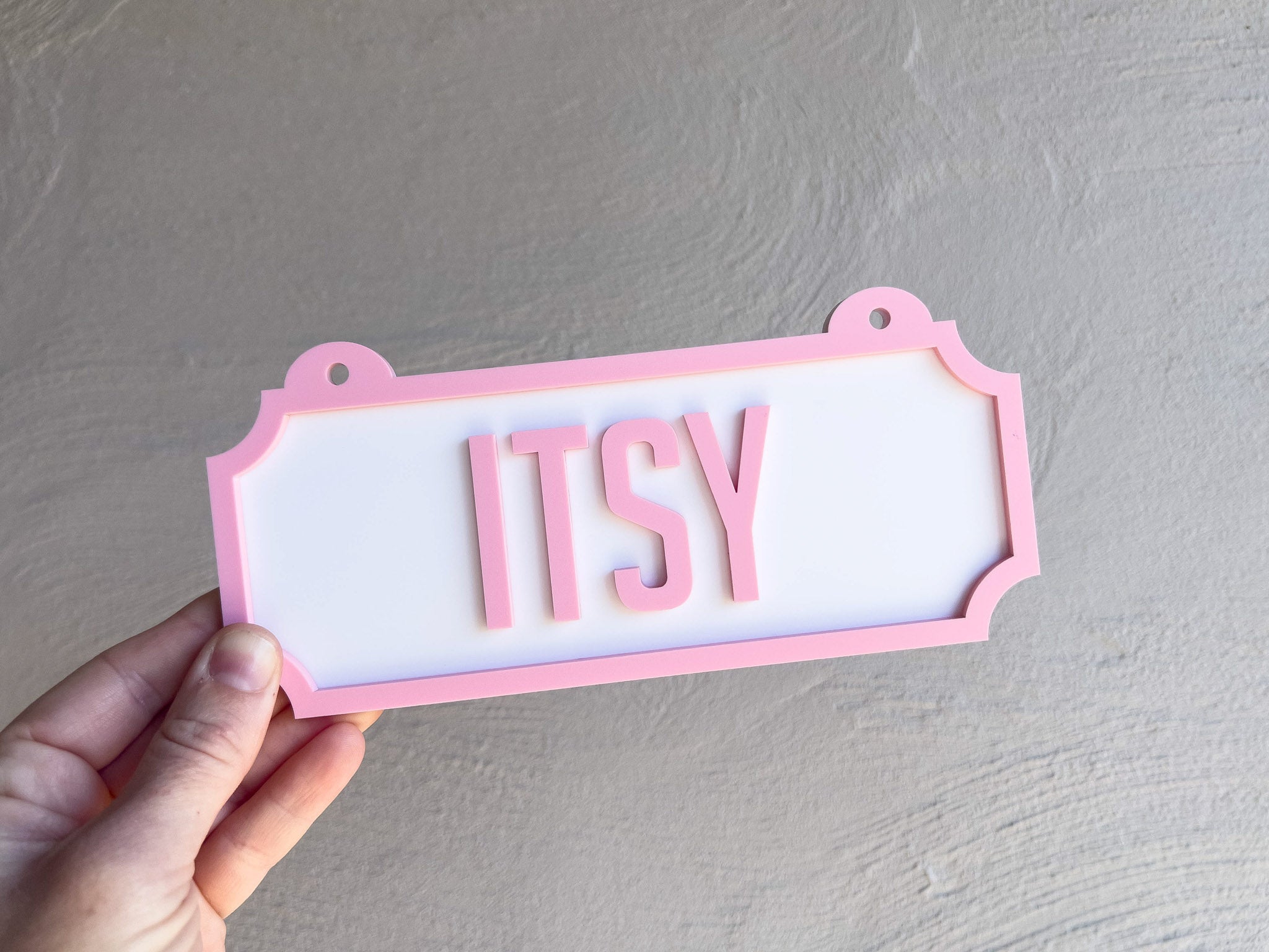 Hand holding a pink and white sign with 'ITSY' text against a grey background | Coji Designs