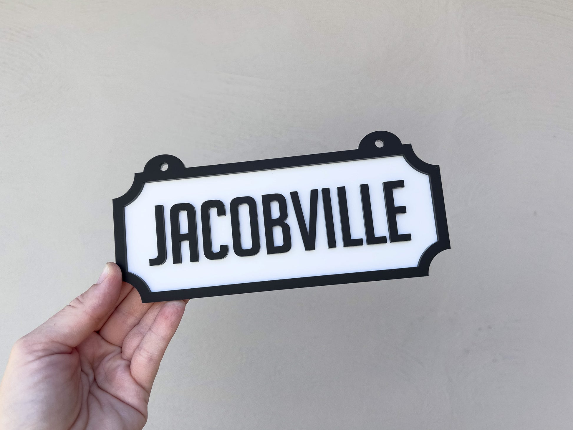 Hand holding a sign with 'JACOBVILLE' text against a plain background | Coji Designs