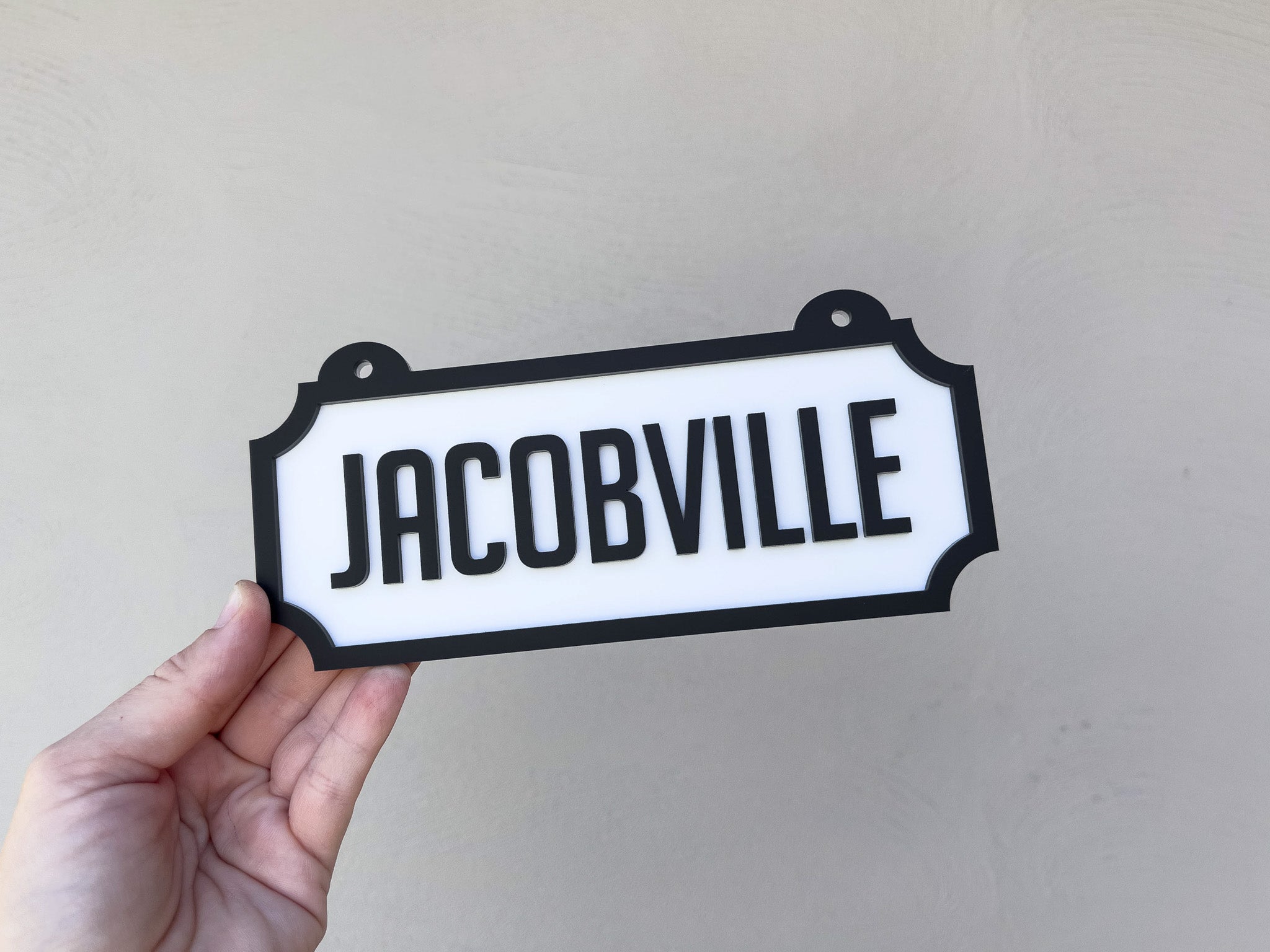 Hand holding a sign with 'JACOBVILLE' text against a plain background | Coji Designs