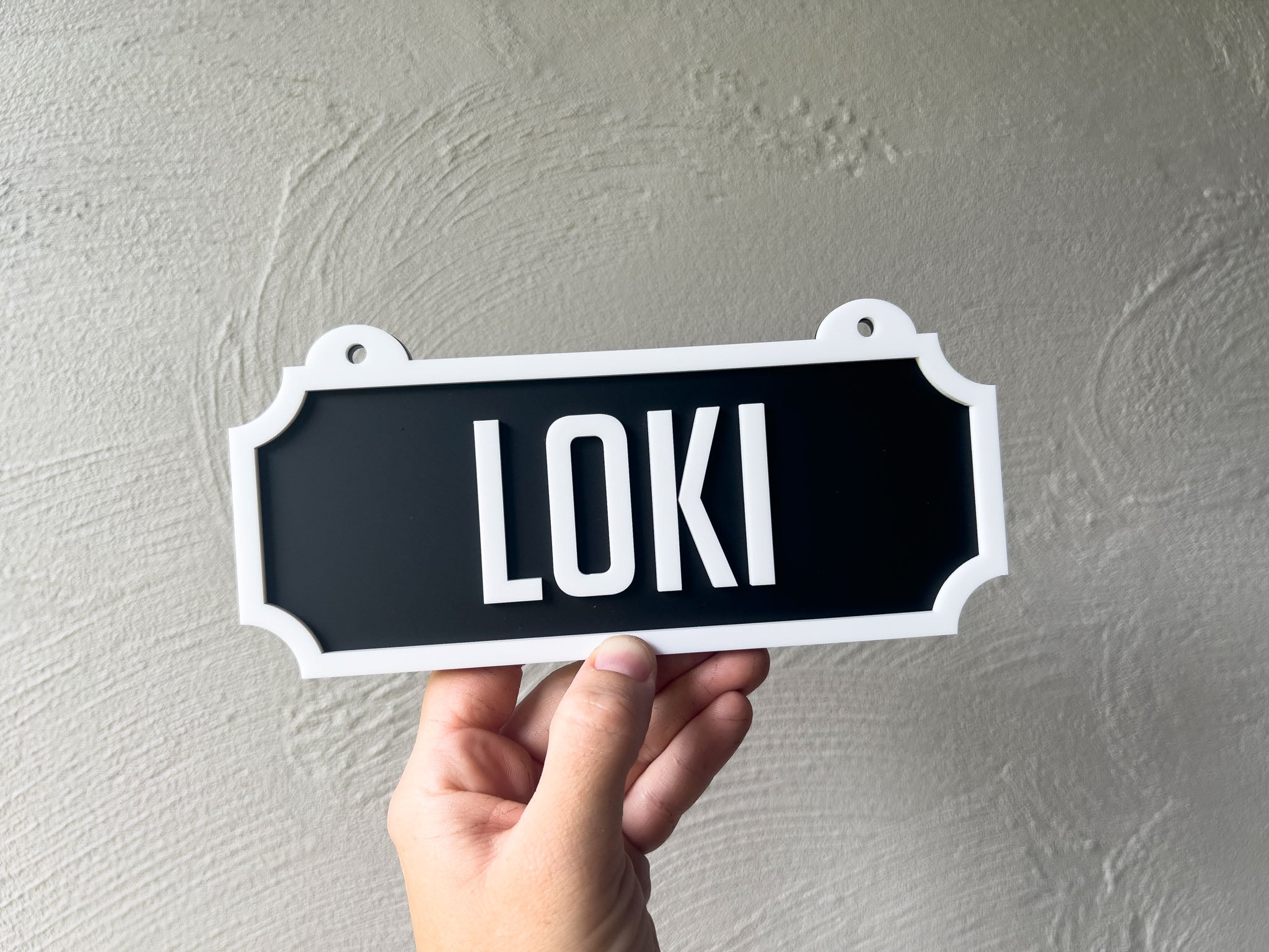Hand holding a black sign with 'LOKI' on a grey background | Coji Designs